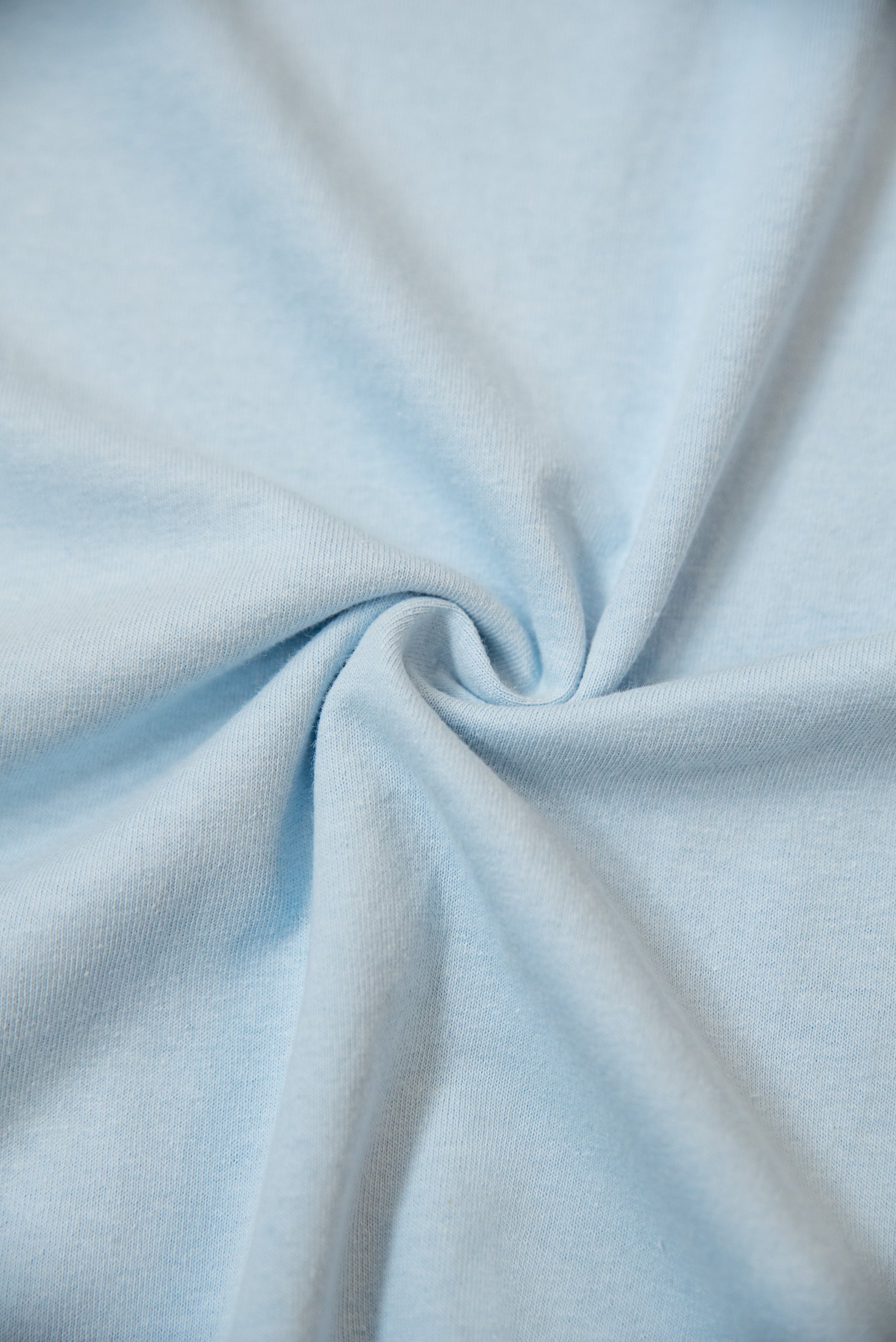 Fabric texture of light blue short sleeved t-shirt, showing soft 100% cotton material with smooth finish and gentle twist.