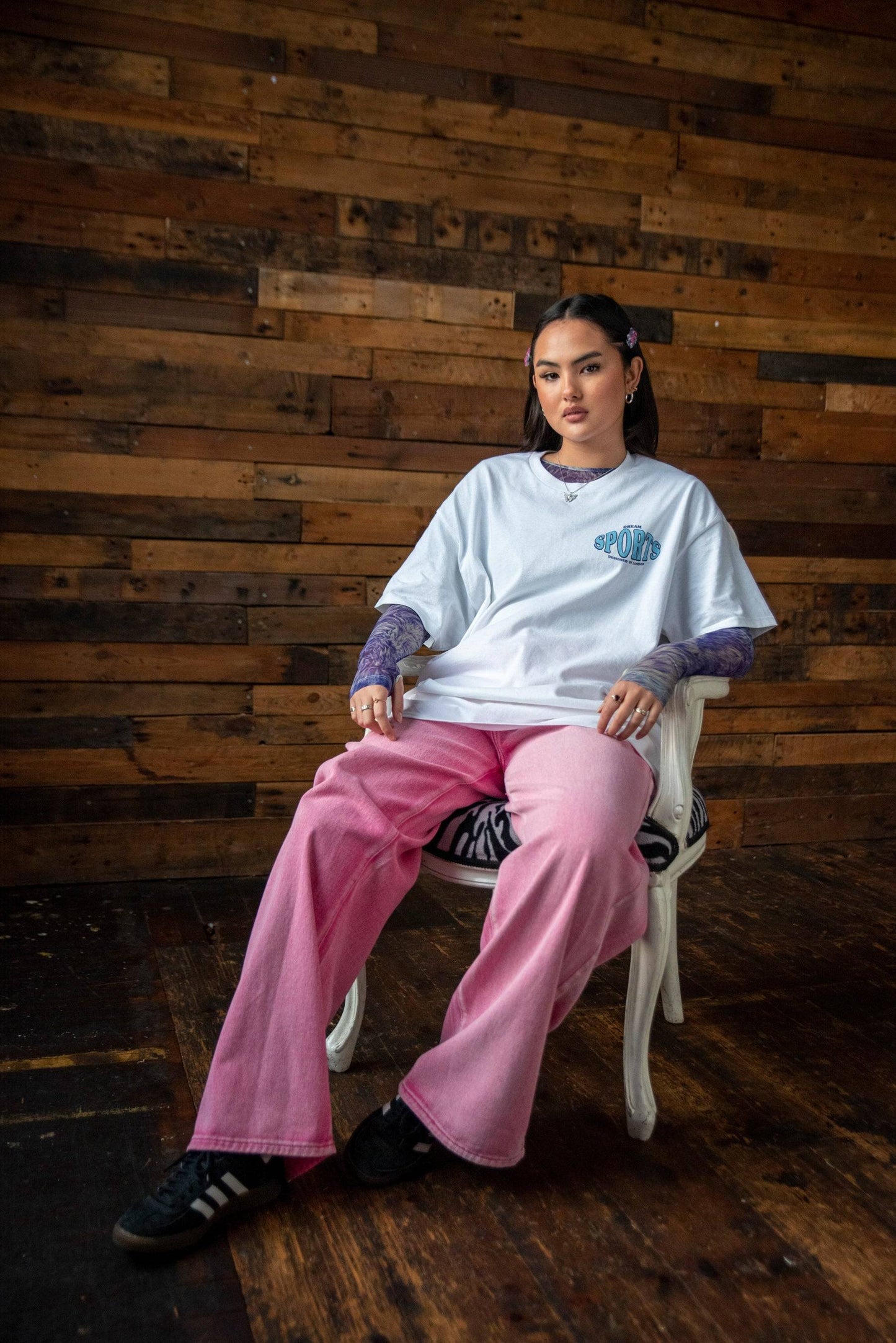 Full-body view of model in white Dream Sports t-shirt and pink trousers, styled for a casual streetwear look.