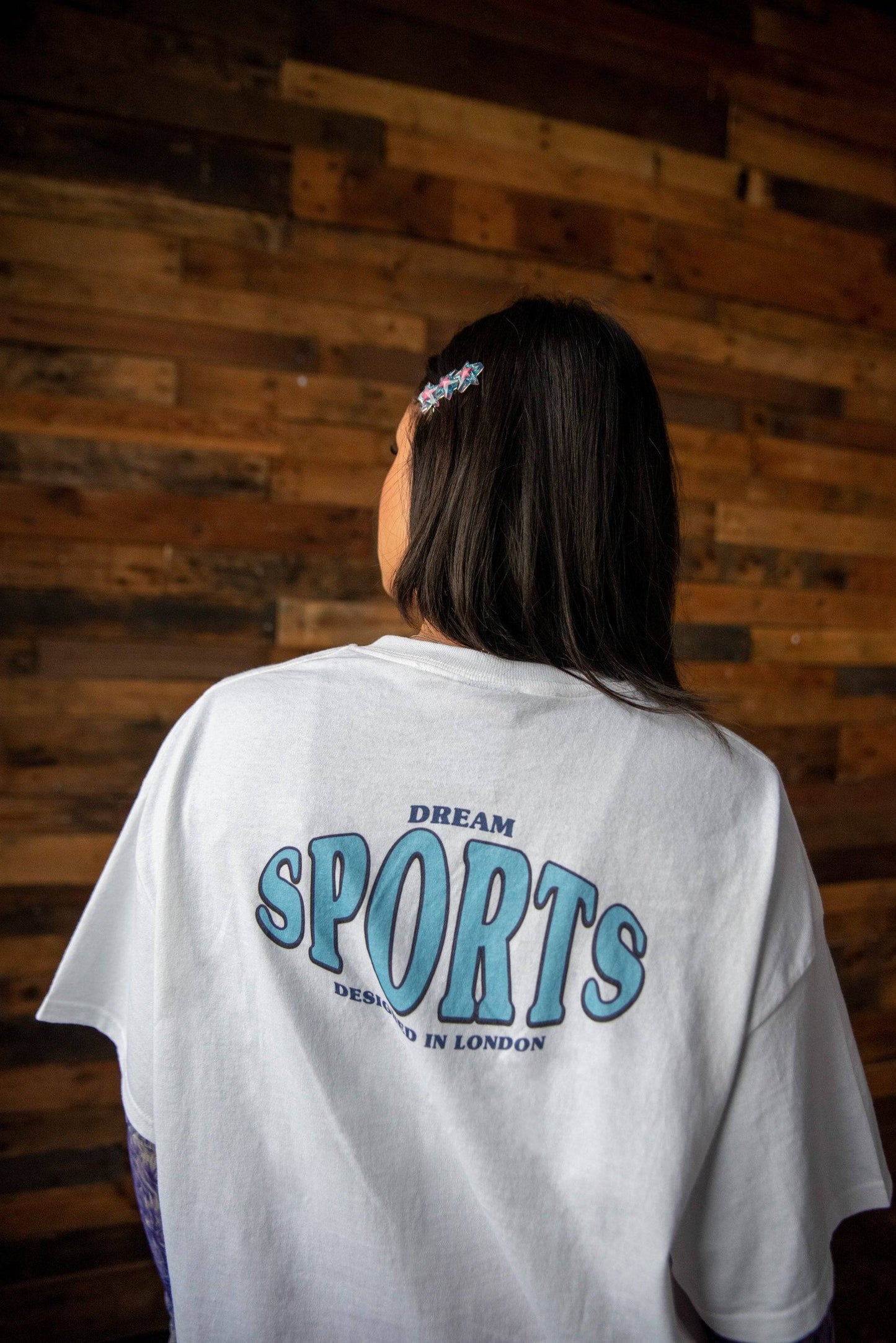 Back view of white graphic t-shirt with large Dream Sports print, showcasing relaxed fit and bold typography design.