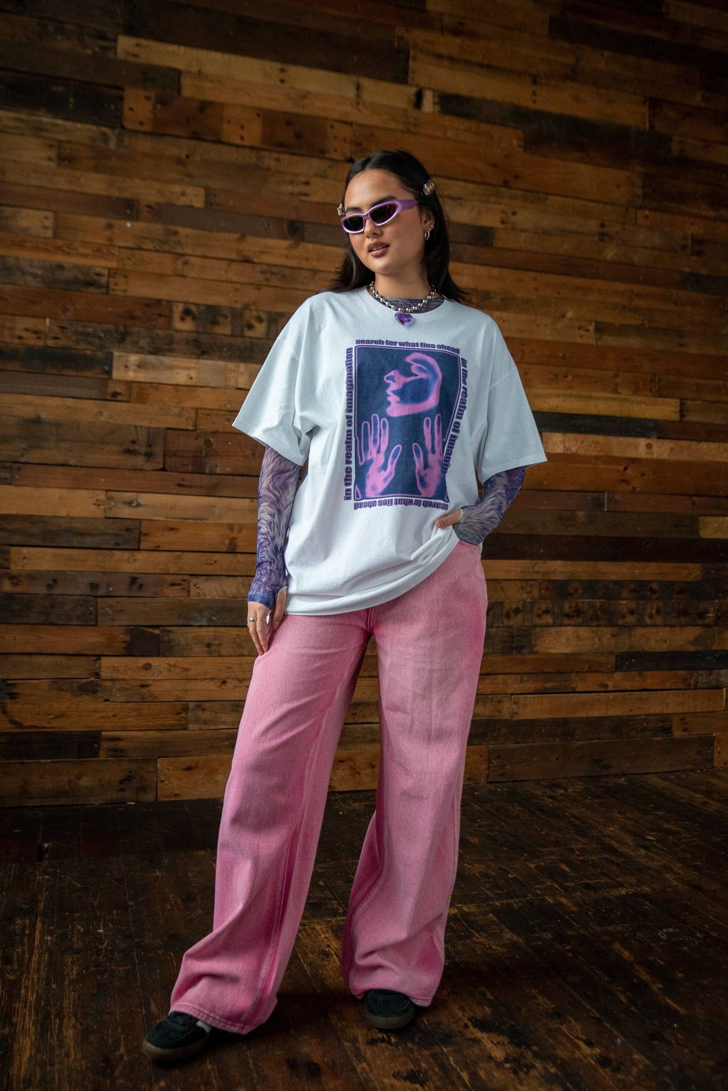 Full outfit featuring Realm Imagination Graphic Cotton T-shirt styled with pink wide-leg pants and layered purple mesh top for a bold streetwear look.