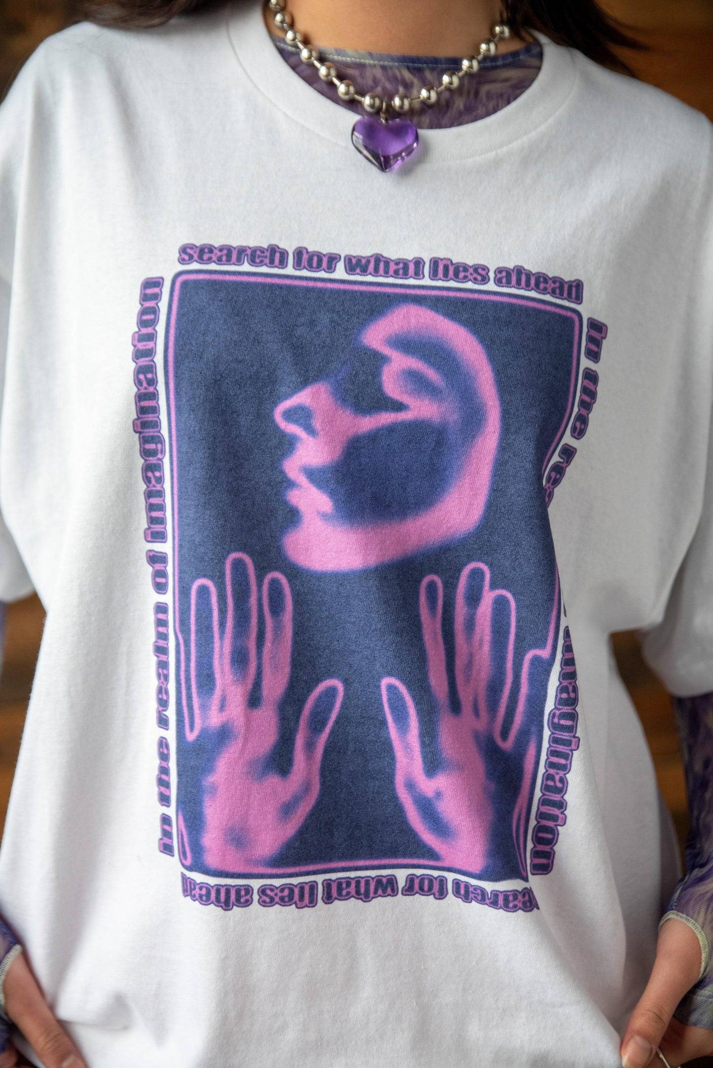 Close-up of the Realm Imagination Graphic Cotton T-shirt showing vivid purple face and hand design with artistic typography on soft white fabric.