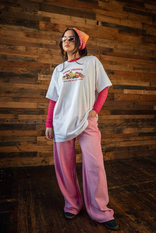 Unisex Short Sleeved White Stay Fruity T-shirt paired with pink pants and layered top. Relaxed fit cotton tee with colorful fruit print.