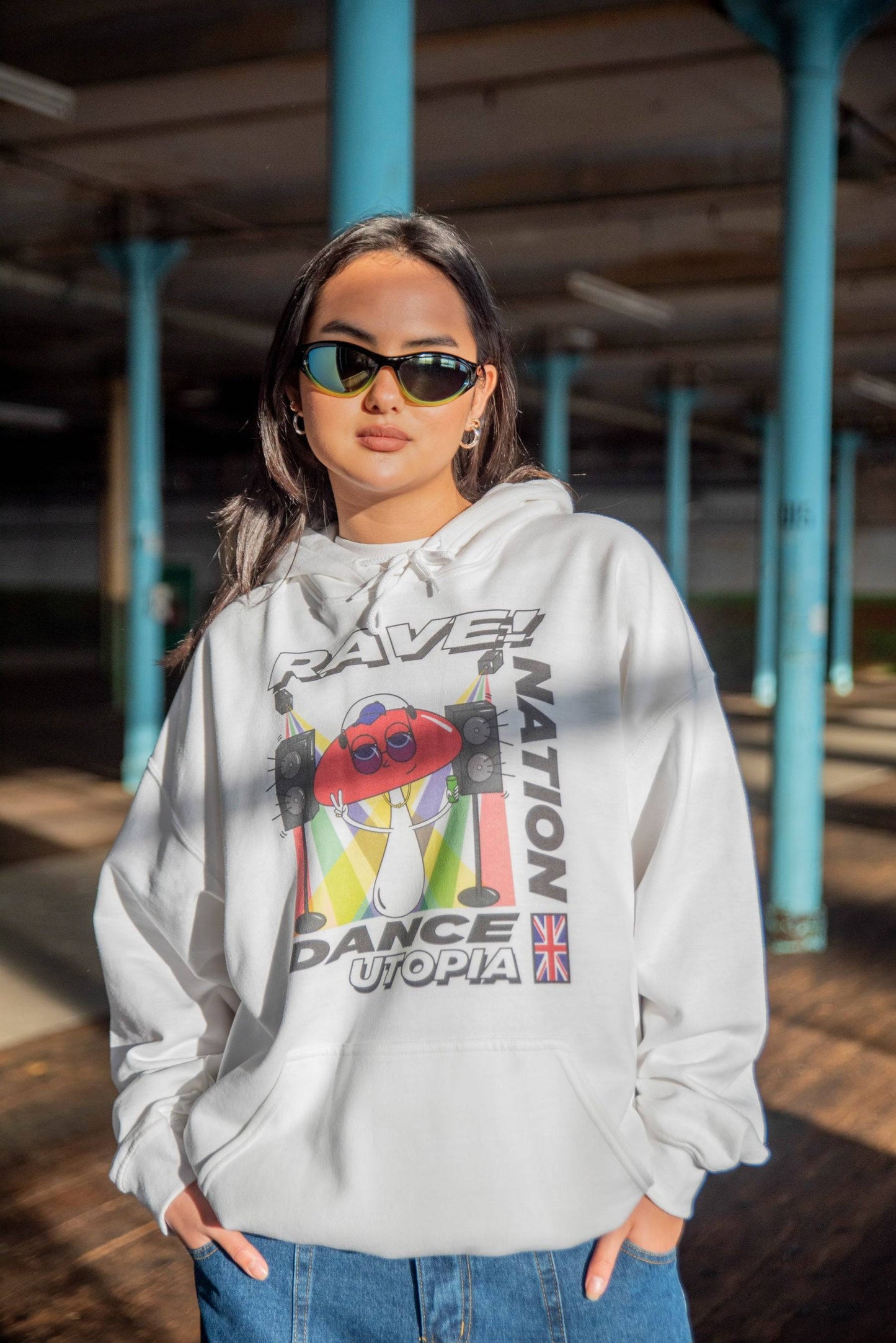 White unisex hoodie featuring Mushroom Dance Utopia print, worn by model in urban setting. Streetwear style with relaxed fit and bold graphic.