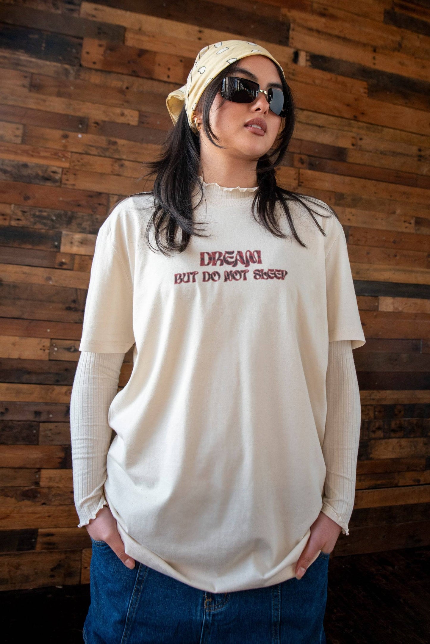 Natural cotton t-shirt with red cursive 'DREAM BUT DO NOT SLEEP' logo print, styled in a relaxed fit over layered sleeves.