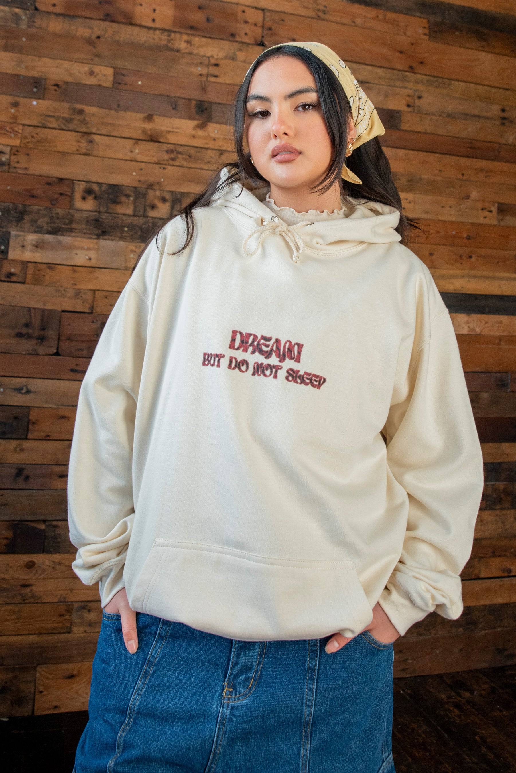 Unisex vanilla hoodie with cursive logo print 'DREAM BUT DO NOT SLEEP', made from heavyweight cotton in a relaxed fit. Styled with a denim skirt.