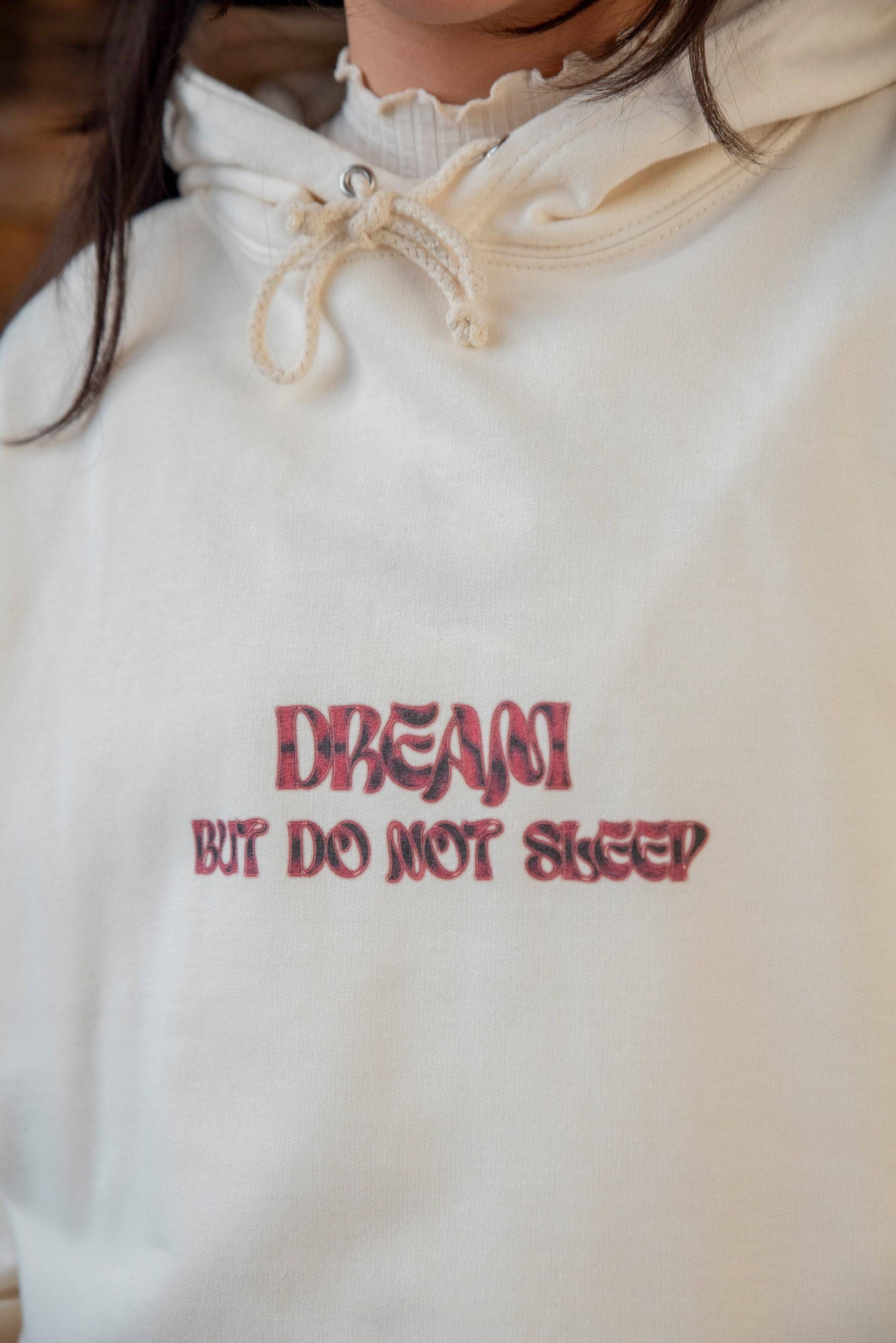 Close-up of vanilla hoodie showing red cursive logo print 'DREAM BUT DO NOT SLEEP' on heavyweight cotton fabric. Ideal for casual wear.