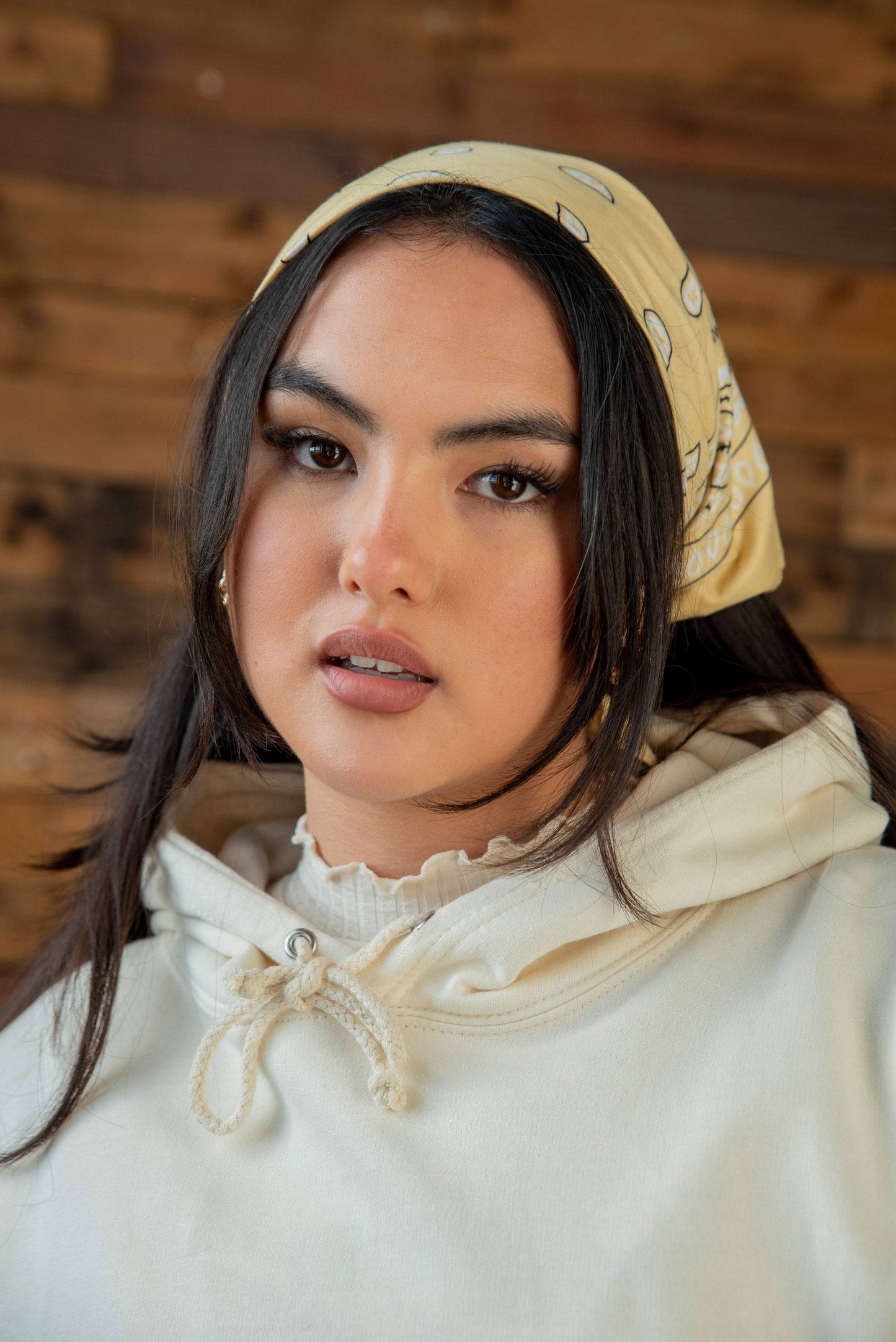 Model wearing vanilla hoodie with drawstring hood and cursive logo, styled with a yellow bandana. Part of unisex streetwear collection.