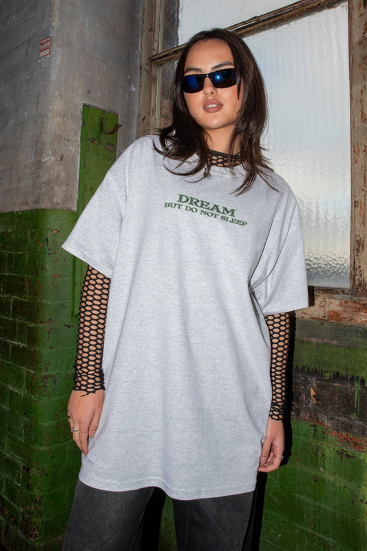 Unisex short sleeve T-shirt in ash grey with futuristic 'DREAM BUT DO NOT SLEEP' logo, styled with fishnet sleeves and dark jeans.