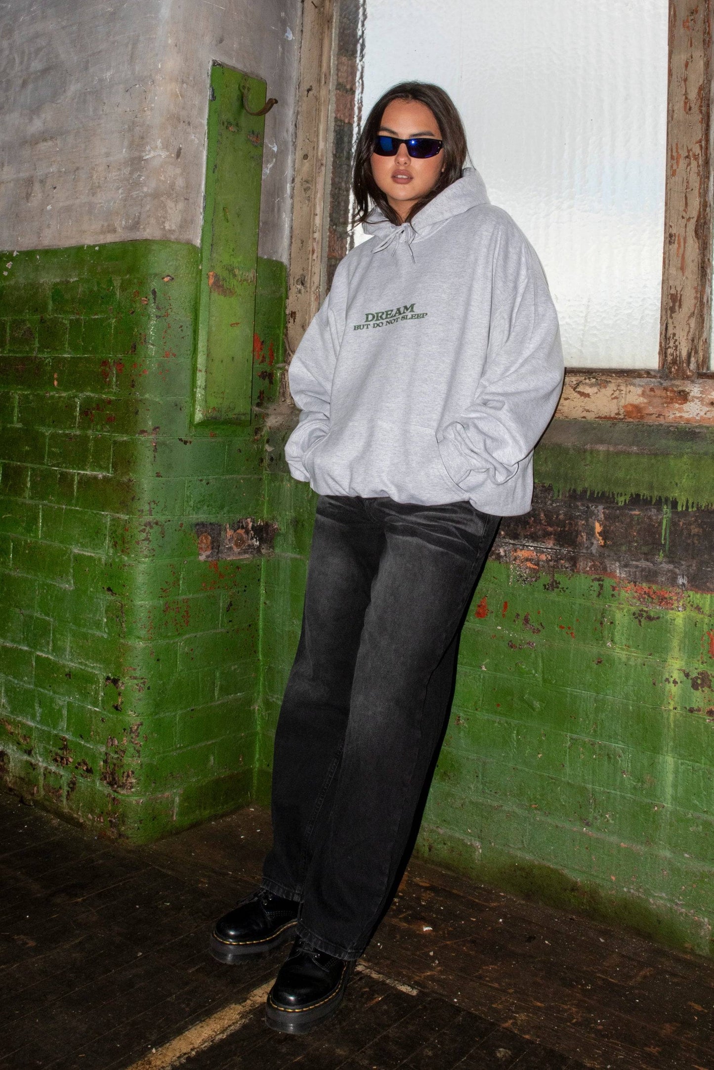 Full-body view of model in ash grey DBDNS hoodie and black jeans. Unisex relaxed fit cotton hoodie styled for Y2K streetwear look.