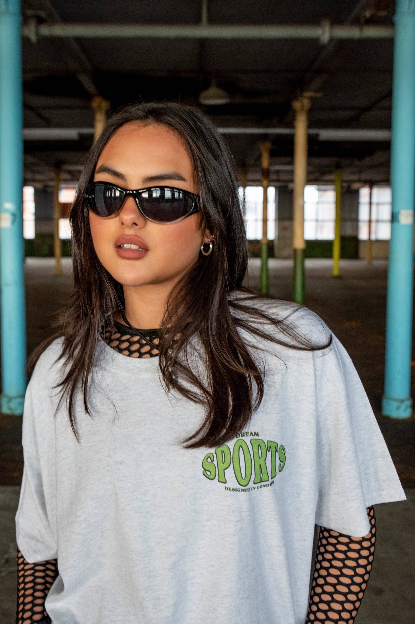 Close-up of Heather Grey T-shirt - Dream Sports Print worn with black fishnet sleeves. Features bold green chest logo and relaxed fit.