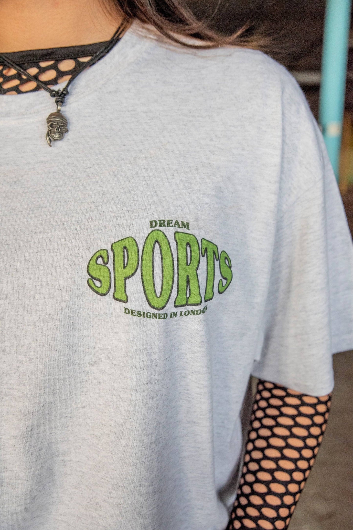 Detailed view of chest logo on Heather Grey T-shirt - Dream Sports Print. Green text reads 'Dream Sports Designed in London'.