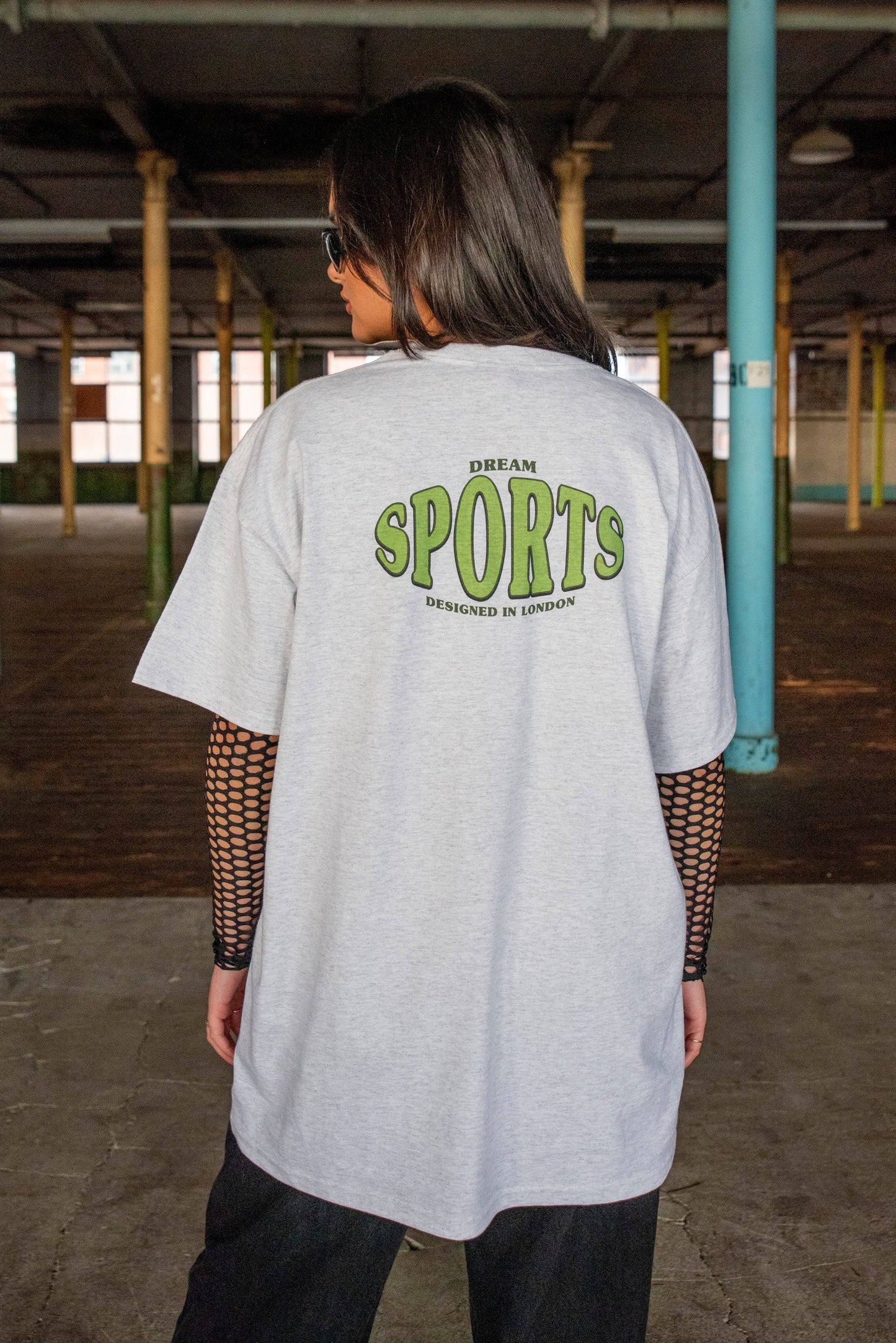 Model wearing Heather Grey T-shirt - Dream Sports Print from the back. Oversized fit with bold green logo and layered styling.