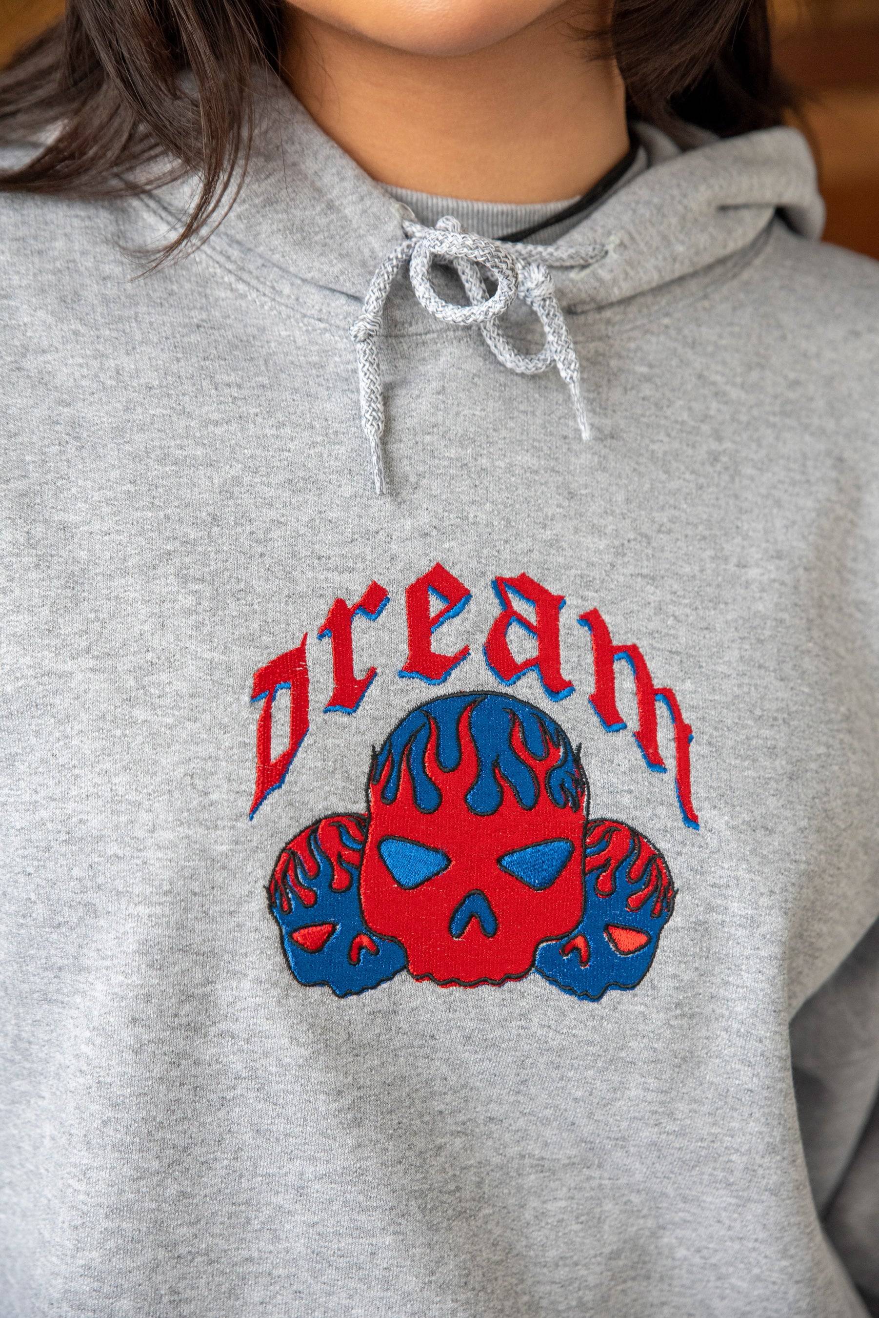 Close-up of Heather Grey Skull Hoodie featuring red and blue flaming skull embroidery with gothic 'dream' lettering on heavyweight cotton fabric.