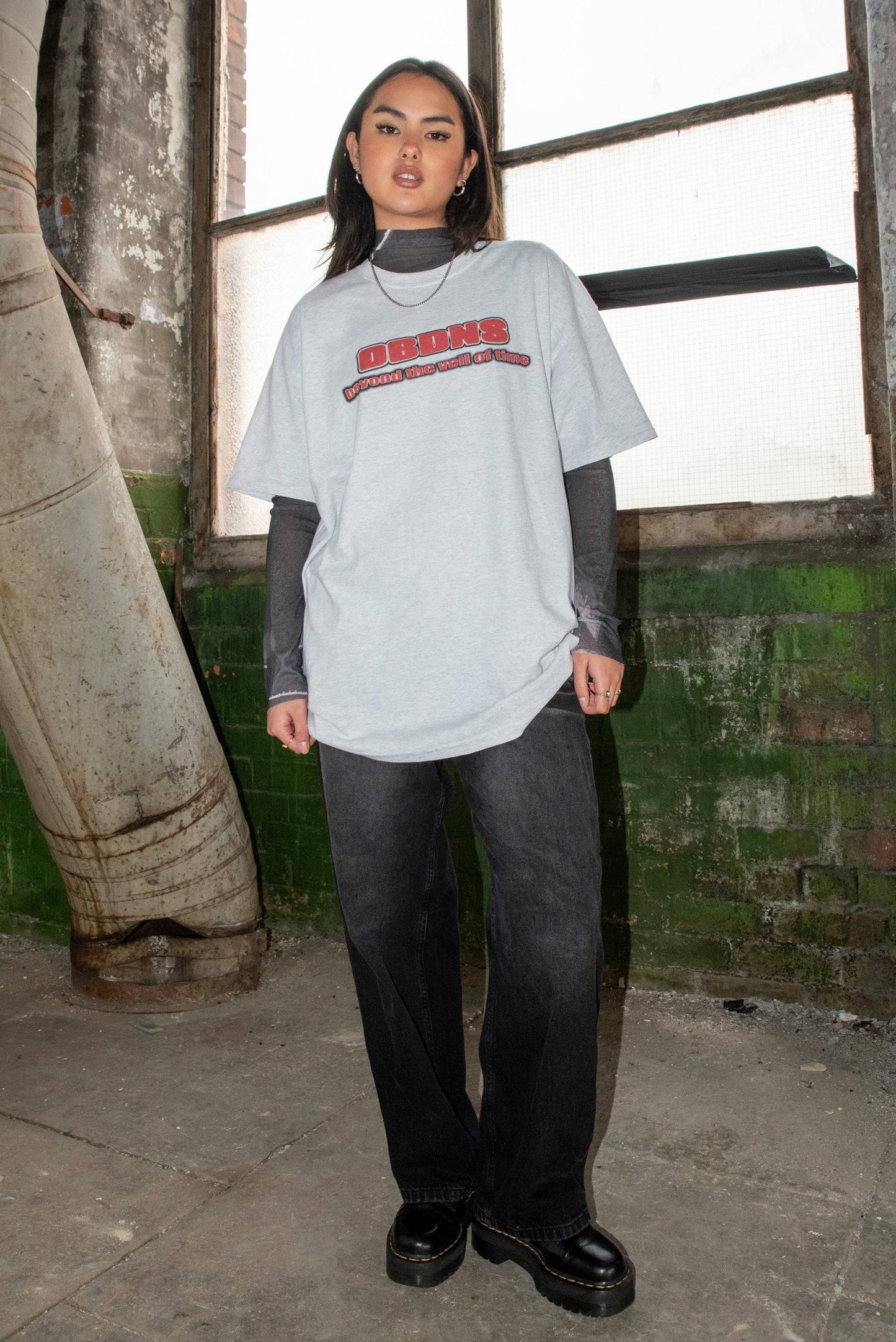 Unisex Ash Grey T-shirt with Logo worn with black jeans and boots, showcasing DBDNS graphic and casual streetwear look.