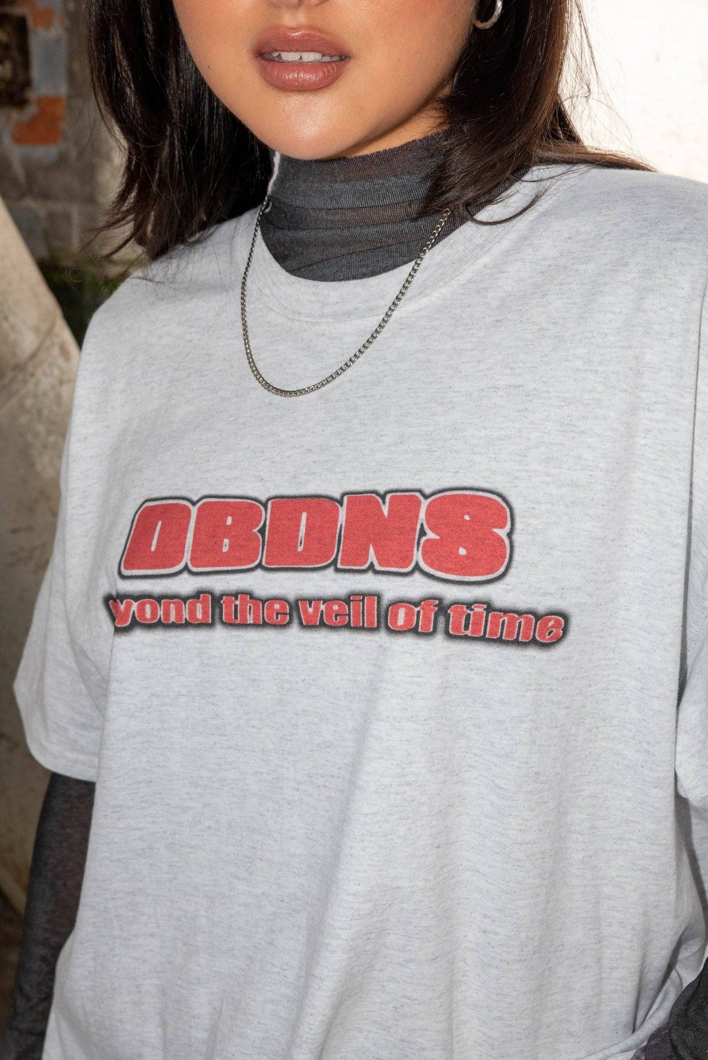 Close-up of Ash Grey T-shirt with bold red DBDNS logo and 'yond the veil of time' text, highlighting cotton texture and print detail.