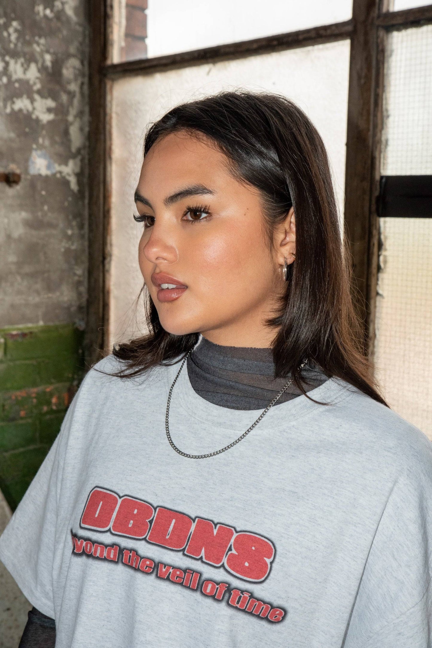 Side view of Ash Grey T-shirt with Logo showing DBDNS graphic and soft cotton fabric, styled with silver chain and layered top.
