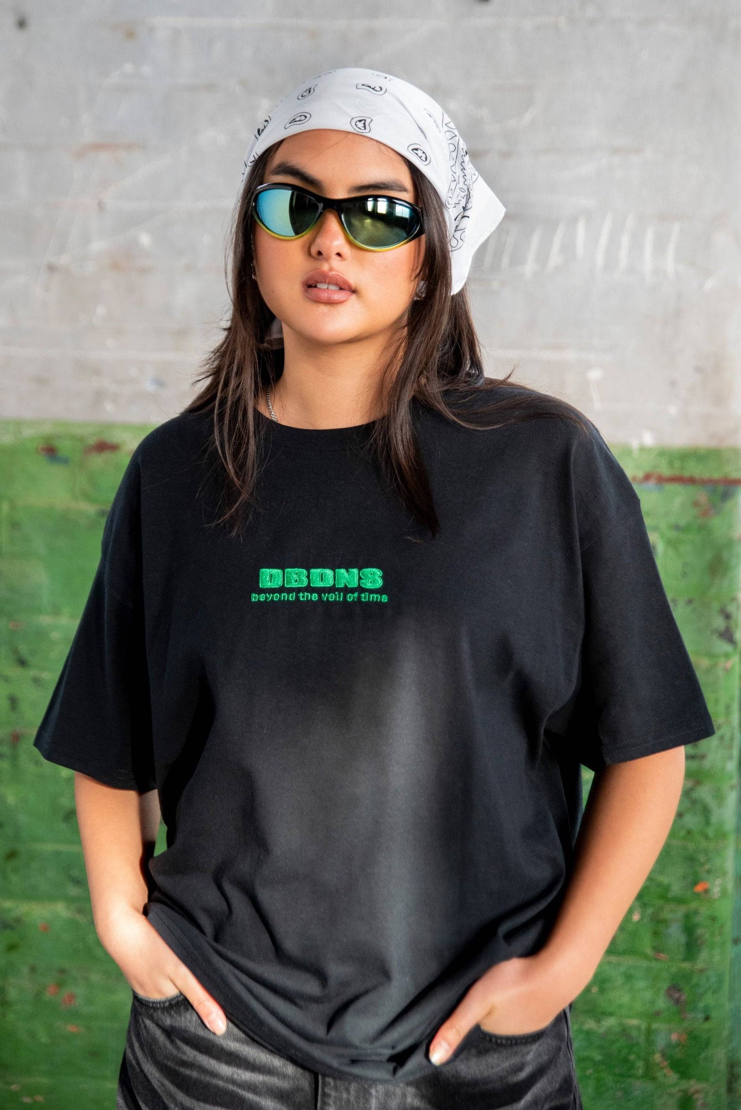 Unisex black short sleeved T-shirt with green DBDNS logo embroidery. Styled with bandana and sunglasses for urban streetwear look.