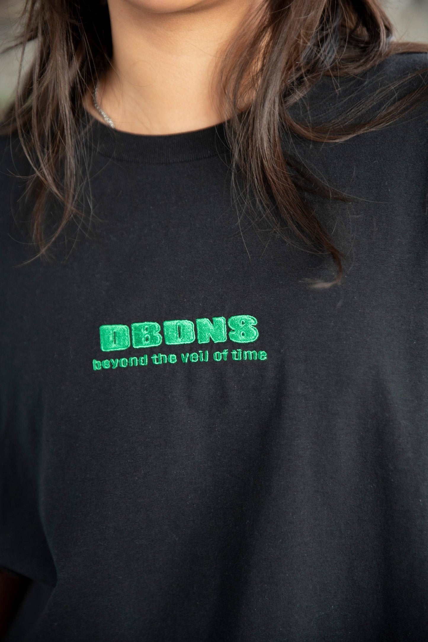 Detailed view of DBDNS logo embroidery on black short sleeved T-shirt. High-quality stitching and soft cotton fabric.
