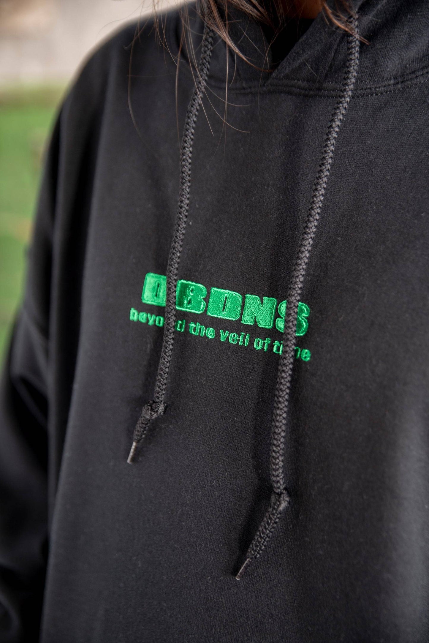 Close-up of DBDNS logo embroidery on black hoodie. Features thick drawstrings and heavyweight cotton fabric for a premium streetwear look.