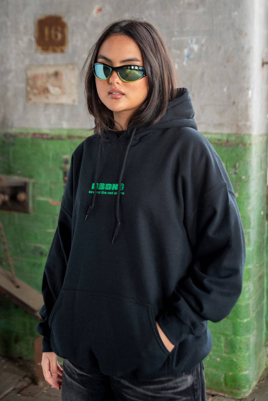 Unisex black hoodie with logo in green embroidery, styled with sunglasses. Heavyweight cotton, ideal for streetwear and y2k fashion.