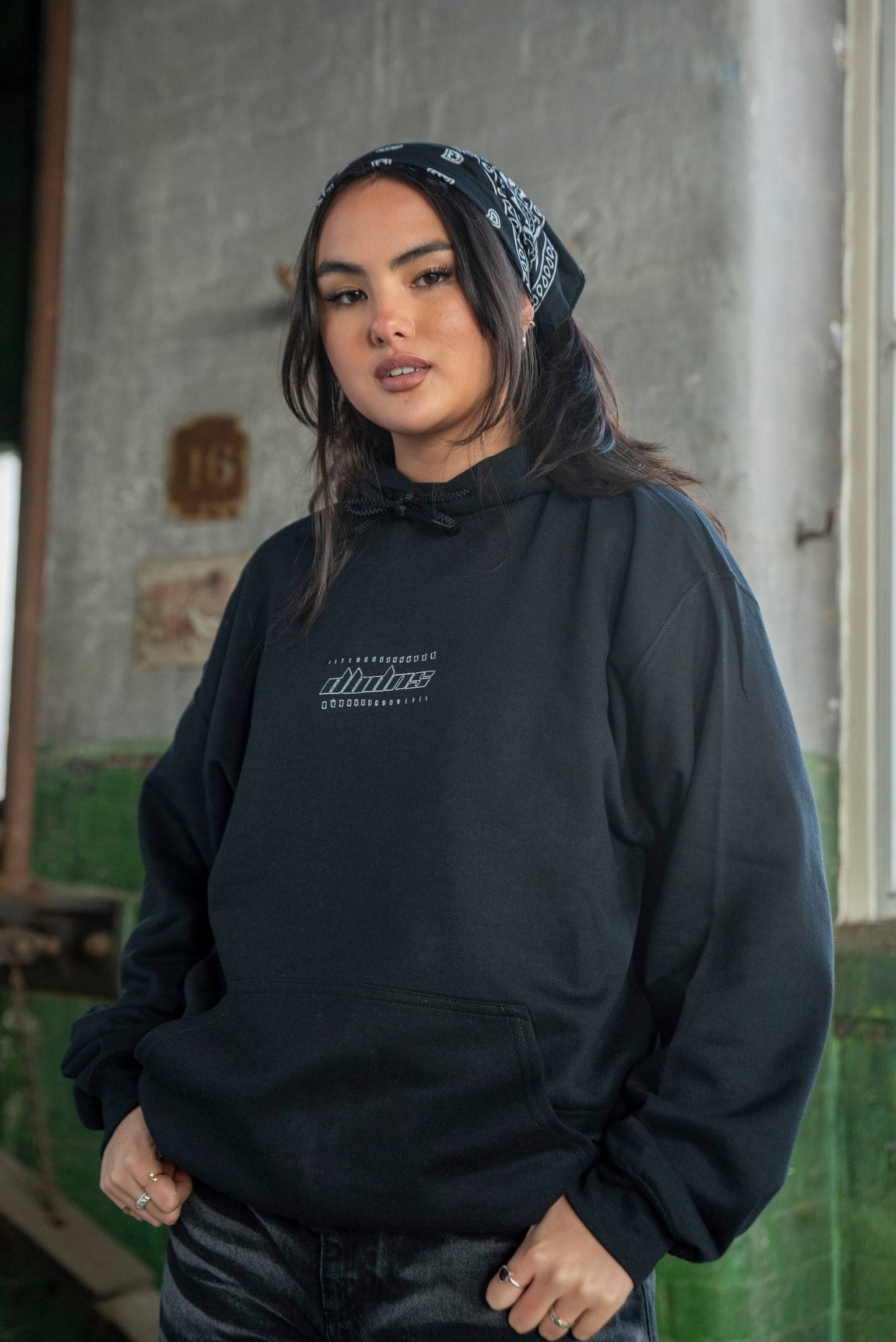 Unisex hoodie black with futuristic logo embroidery, relaxed fit in heavyweight cotton. Styled with streetwear for casual urban look.