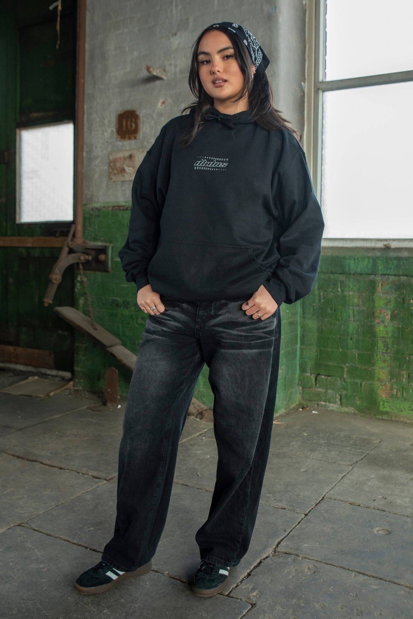 Black unisex hoodie with futuristic logo, styled with wide-leg jeans and sneakers. Heavyweight cotton ideal for streetwear fashion.