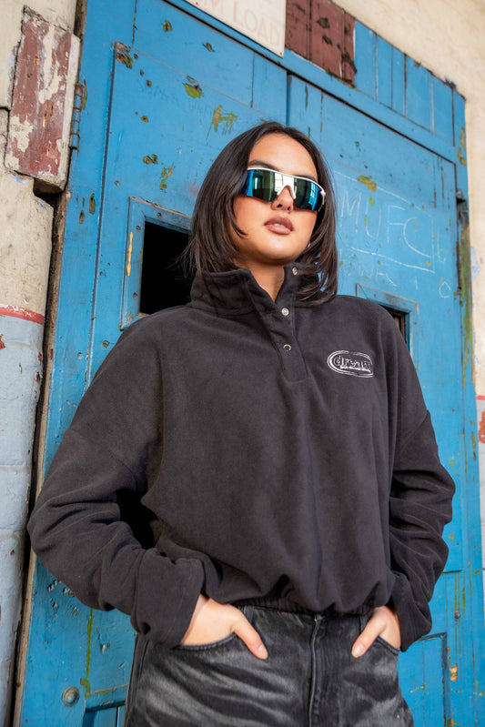 Black Cropped Fleece Sweatshirt with Oval Logo embroidery worn by model in urban setting. Relaxed fit fleece ideal for casual streetwear.