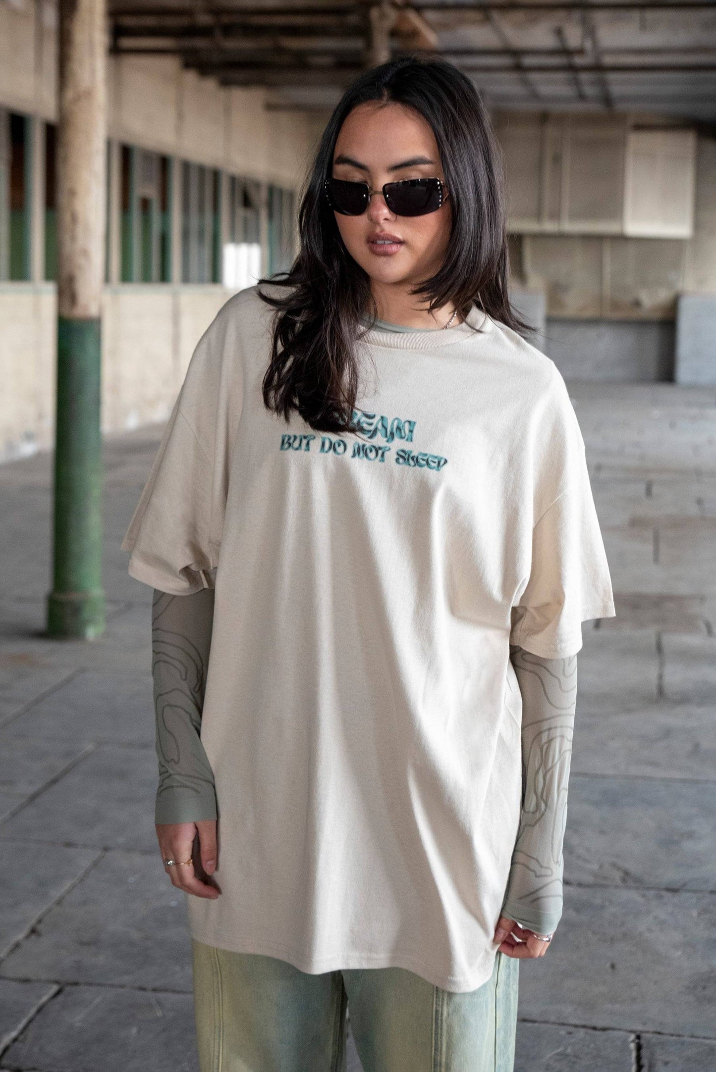 Short Sleeved T-Shirt in Sand - Unisex Cotton Tee styled with layered sleeves and sunglasses, featuring a relaxed fit and cursive logo print.