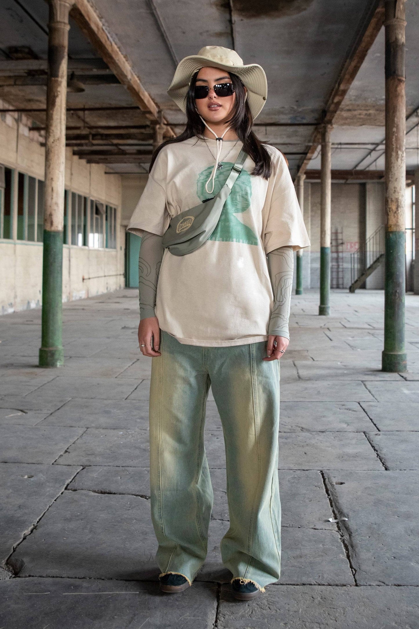 Unisex Graphic Tee in sand styled with wide-leg jeans, layered sleeves, and accessories, showcasing relaxed fit and bold front print.