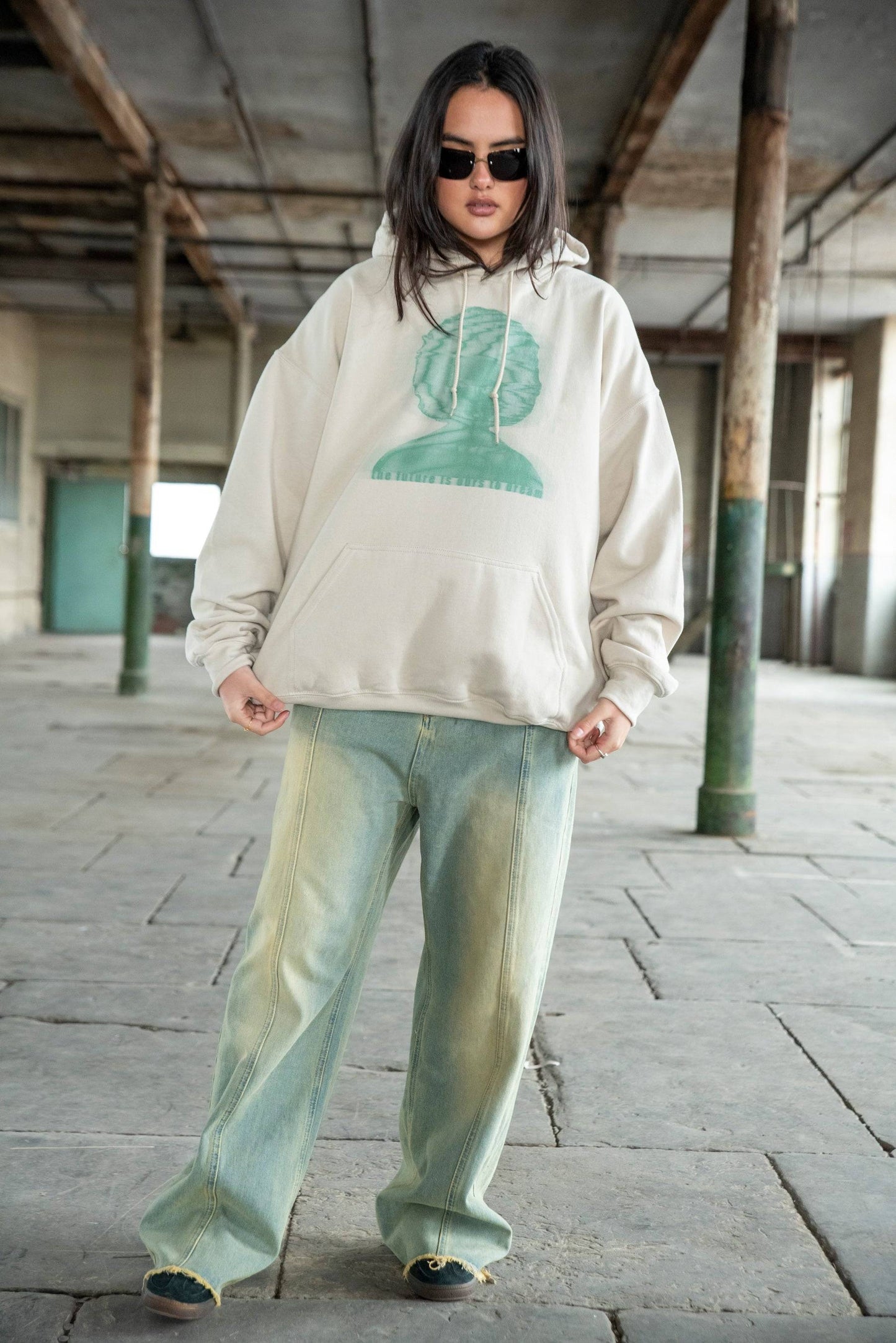 Full-body view of unisex sand hoodie with future-themed print, paired with wide-leg faded jeans for a relaxed streetwear outfit.