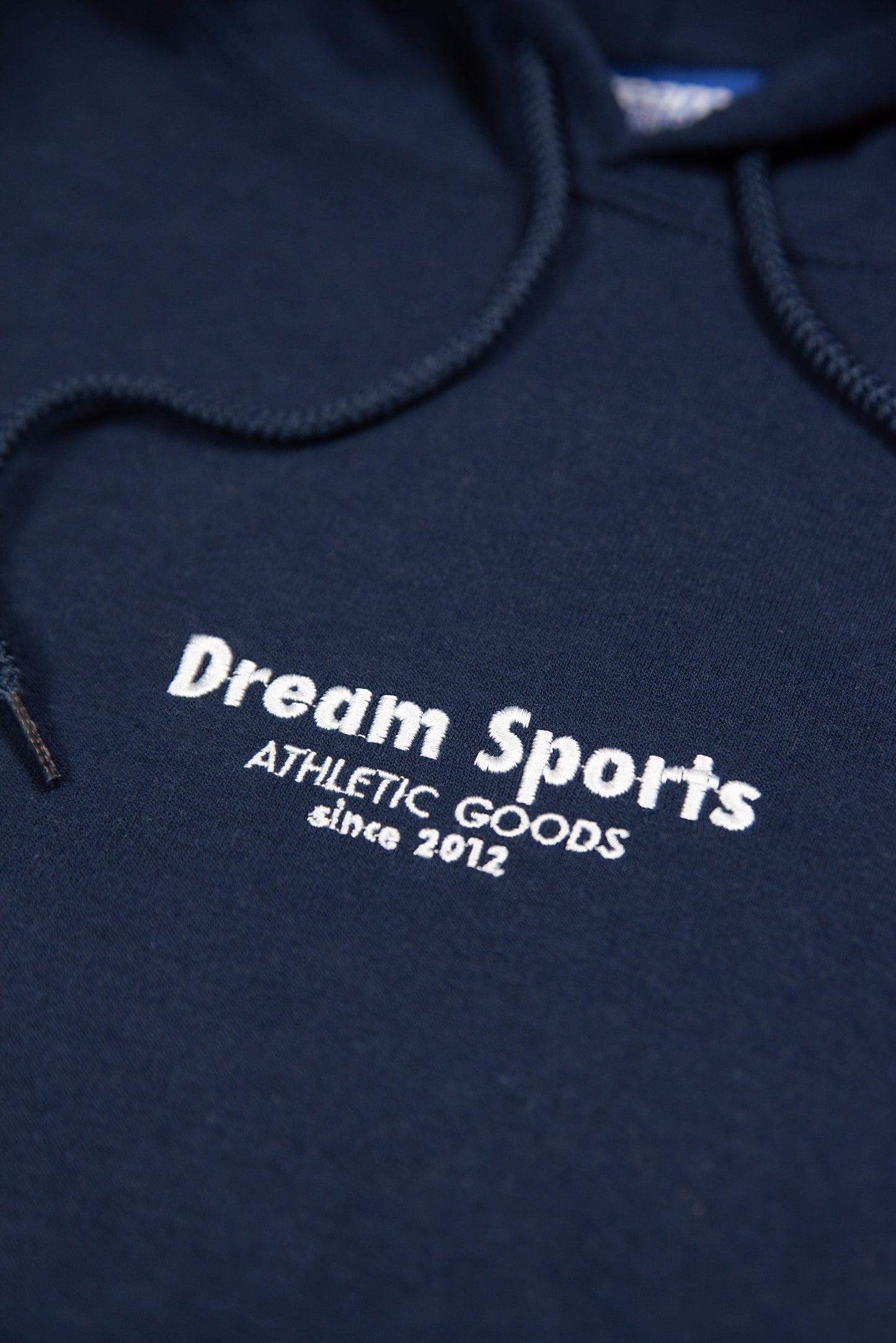 Detailed view of Dream Sports tonal logo embroidery on navy hoodie, showcasing high-quality cotton texture and branding.
