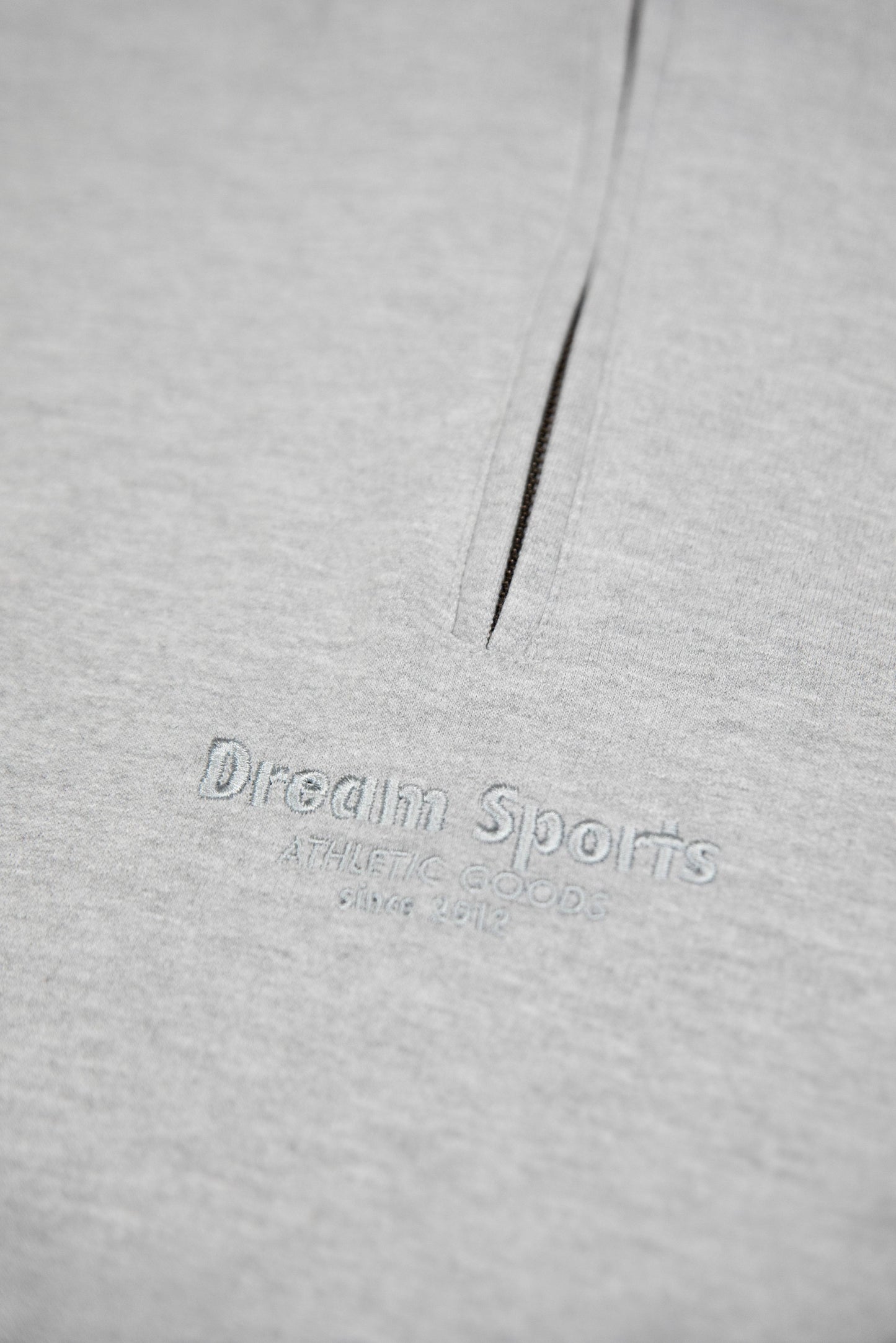Detailed view of Dream Sports tonal logo embroidery on heavyweight cotton fabric of Heather Grey 1/4 zip sweatshirt.