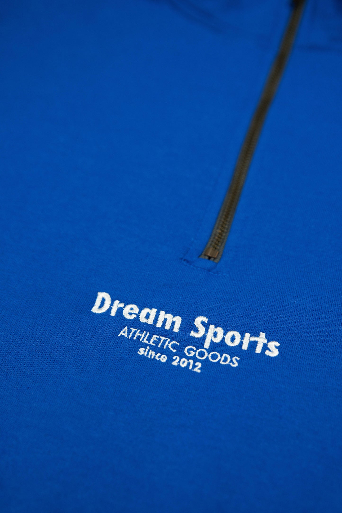 Detailed embroidery of Dream Sports logo on royal blue 1/4 zip sweatshirt, showcasing quality craftsmanship and athletic-inspired branding.