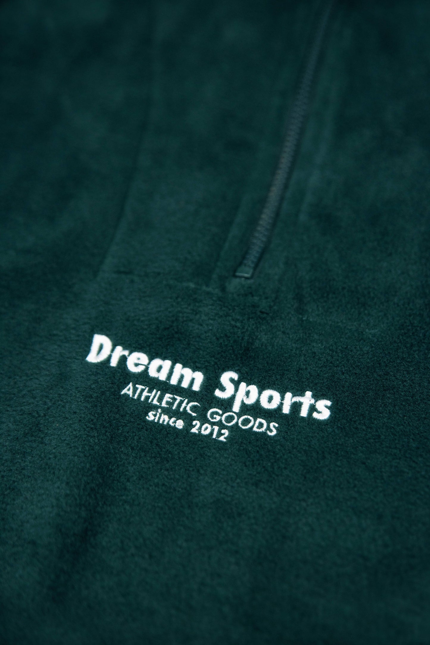 Detailed view of Dream Sports tonal logo embroidery on forest green fleece, highlighting premium stitching and soft texture.