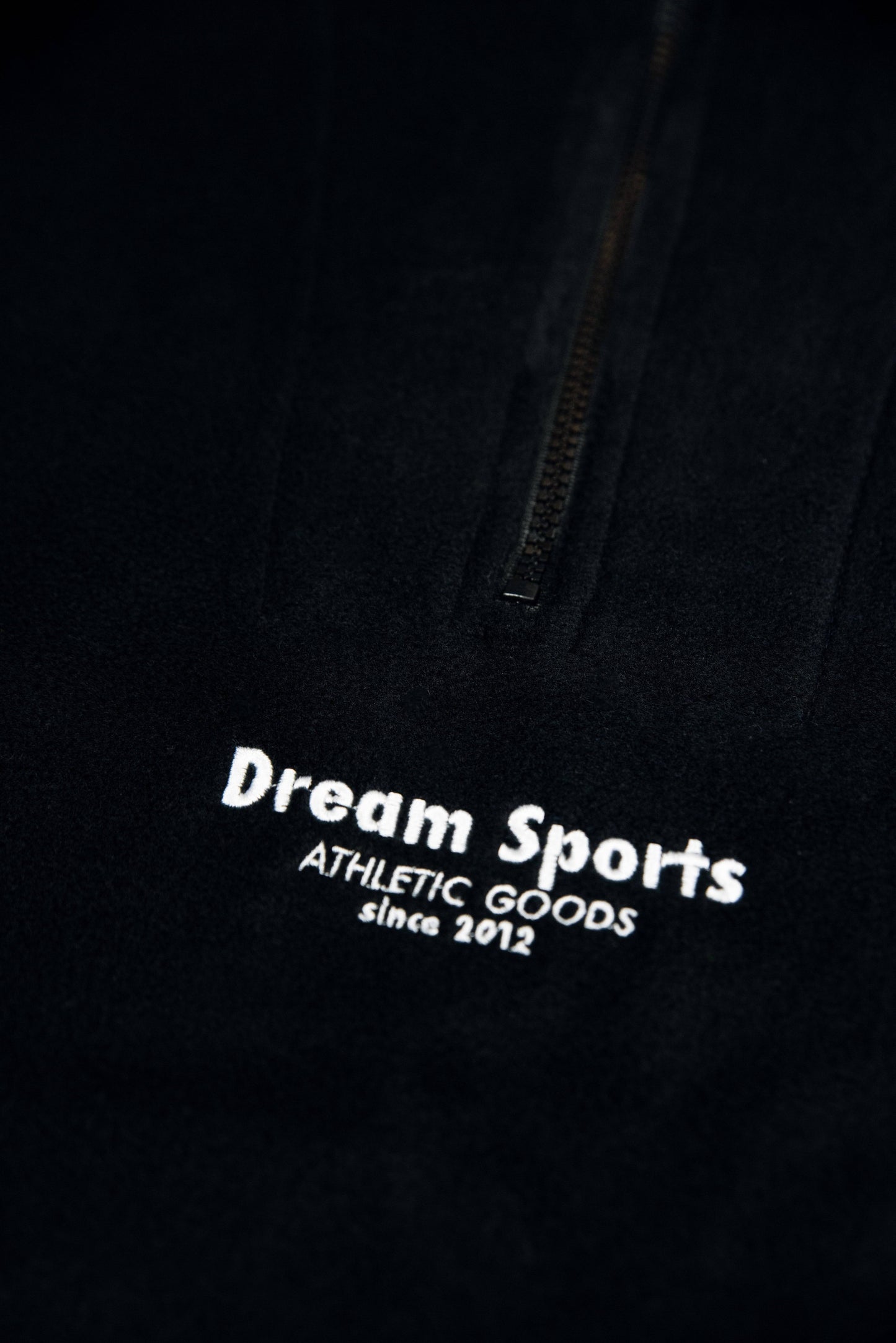 Detailed embroidery of Dream Sports logo on black fleece, emphasizing craftsmanship and minimalist design for modern outerwear appeal.