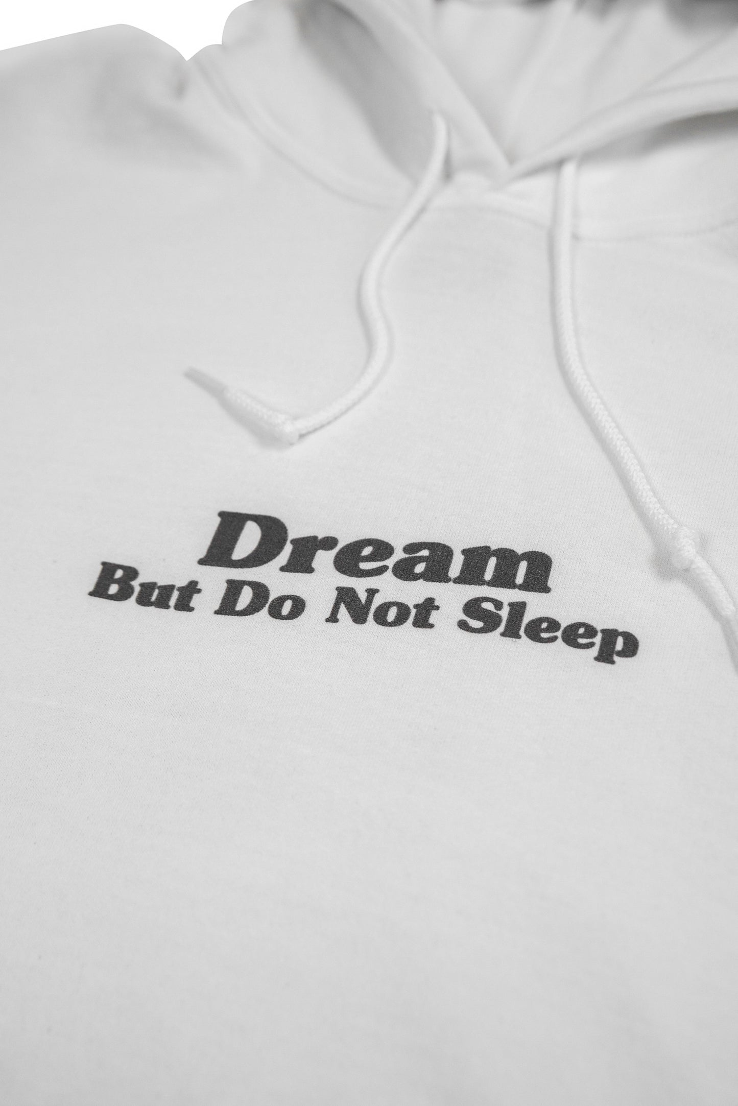 Zoomed-in front print of white hoodie showing 'Dream But Do Not Sleep' slogan in bold black font, made for comfort and everyday inspiration.