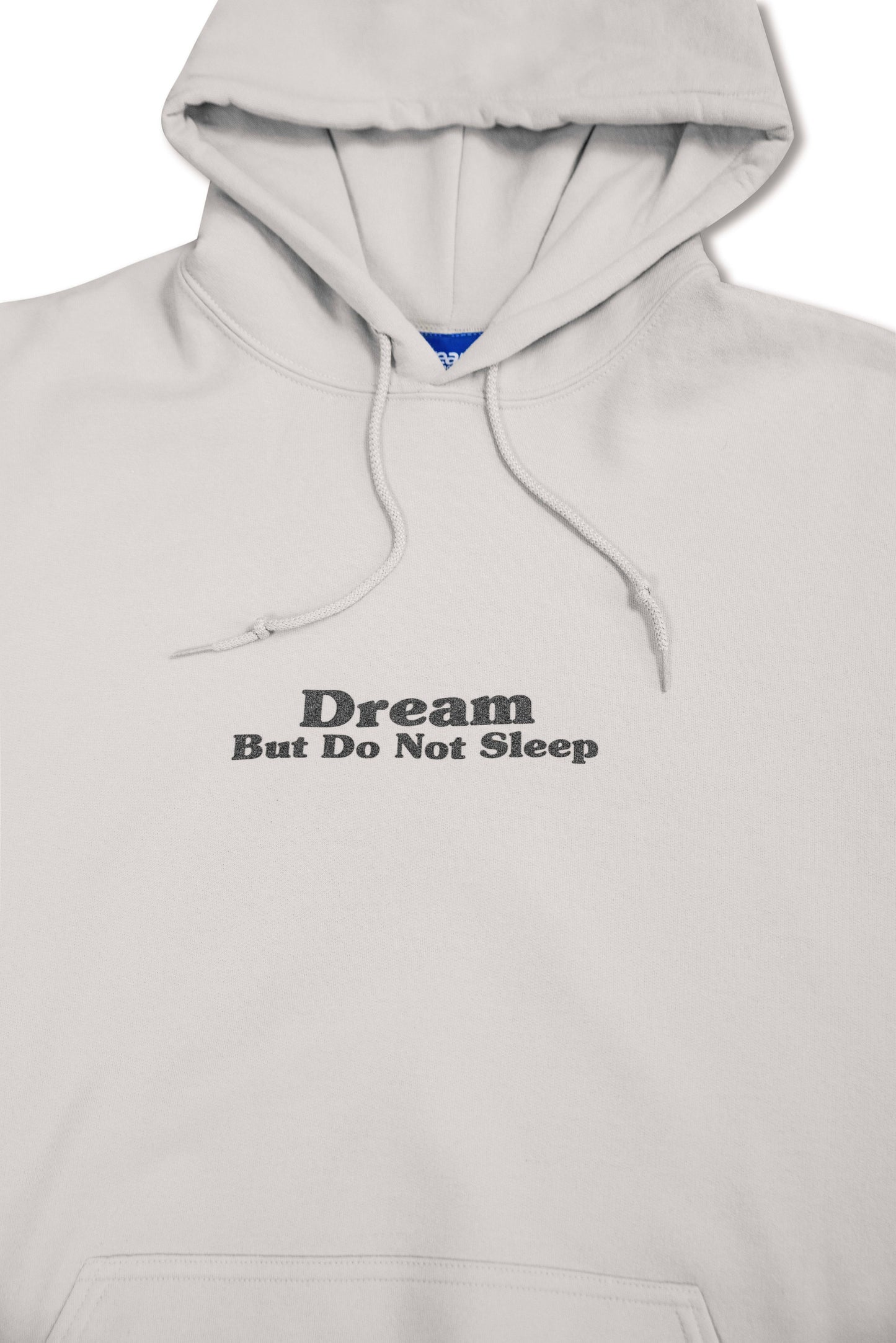 Zoomed-in front chest print reading 'Dream But Do Not Sleep' on sand-colored hoodie. Minimalist streetwear design from DBDNS Shop.