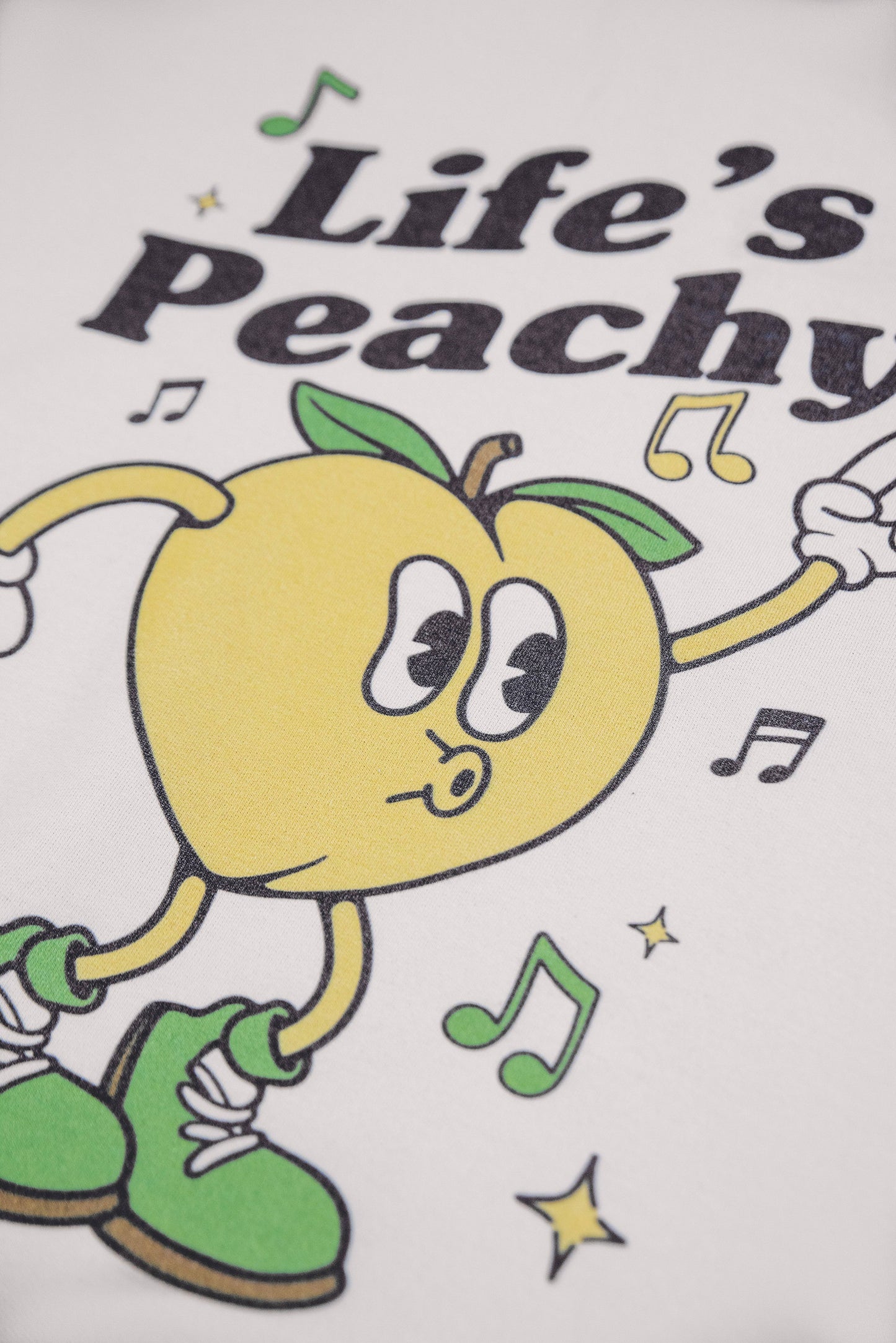 Detailed view of Life's Peachy cartoon peach graphic on unisex sand hoodie. Y2K-inspired design with bold colors and playful typography.