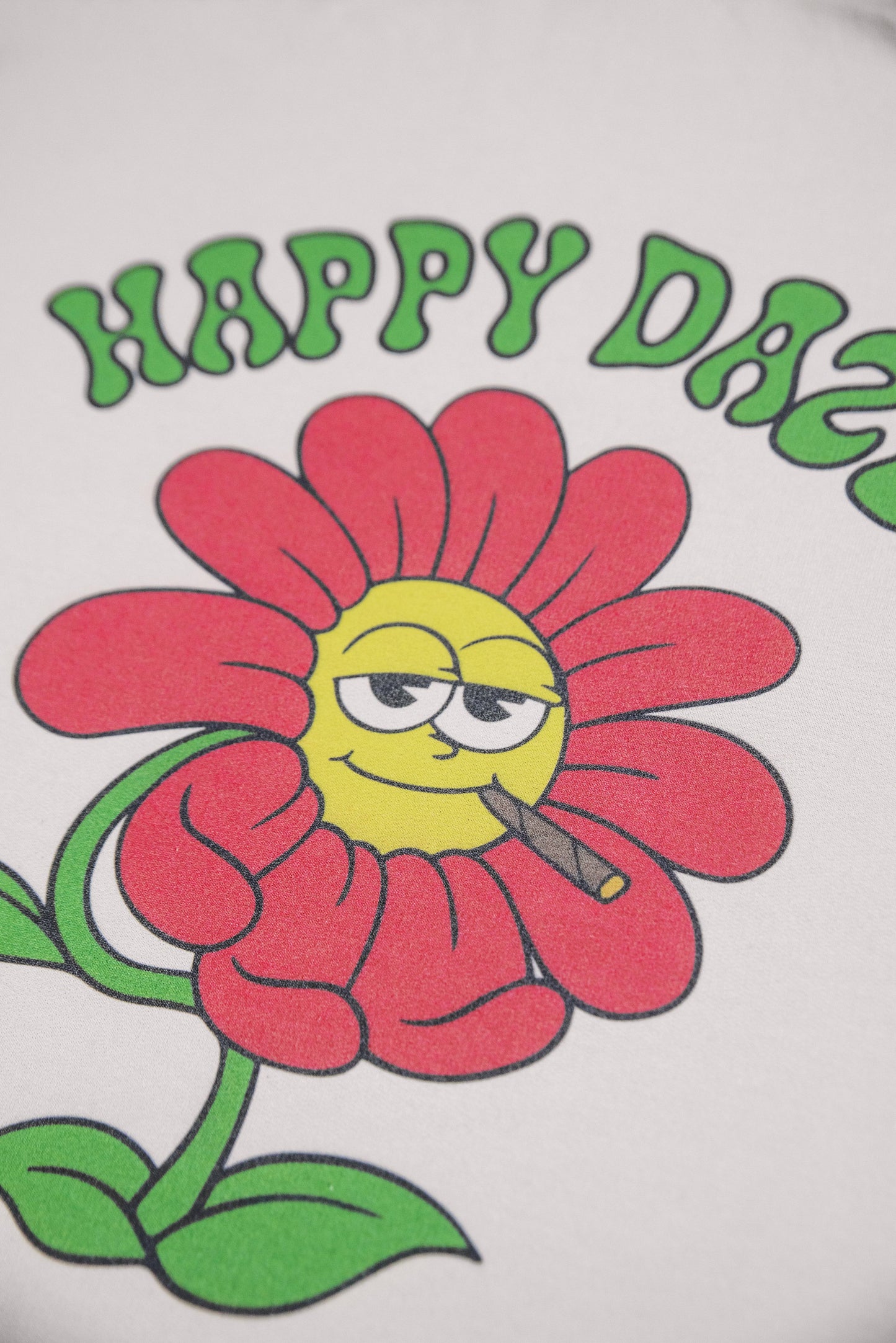 Detailed view of flower graphic on sand hoodie back, showing cartoon flower smoking with 'Happy Daze' text. Bold and playful print.