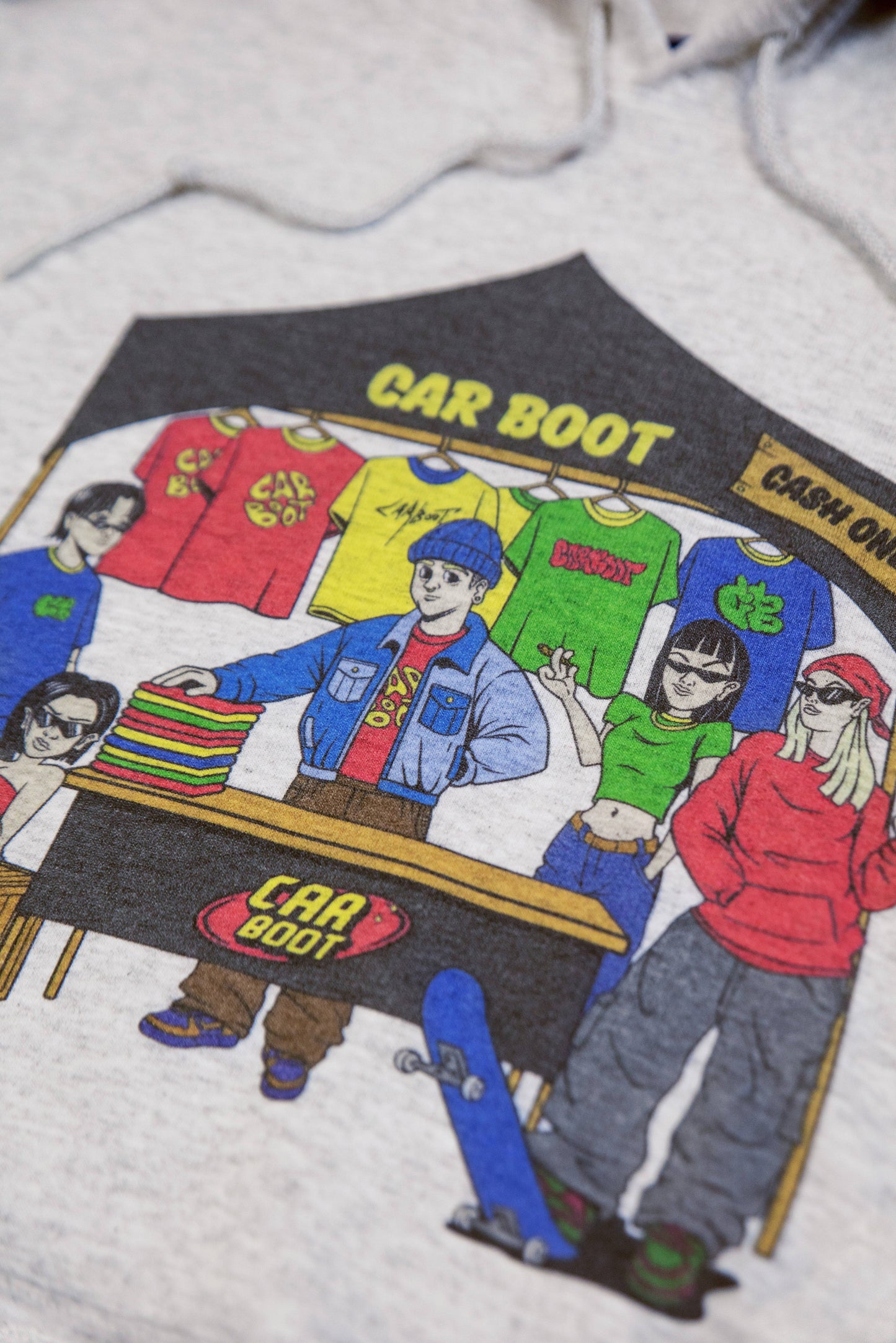 Detailed view of car boot market stall print on ash grey unisex hoodie, showcasing streetwear characters and bold colors for a Y2K aesthetic.