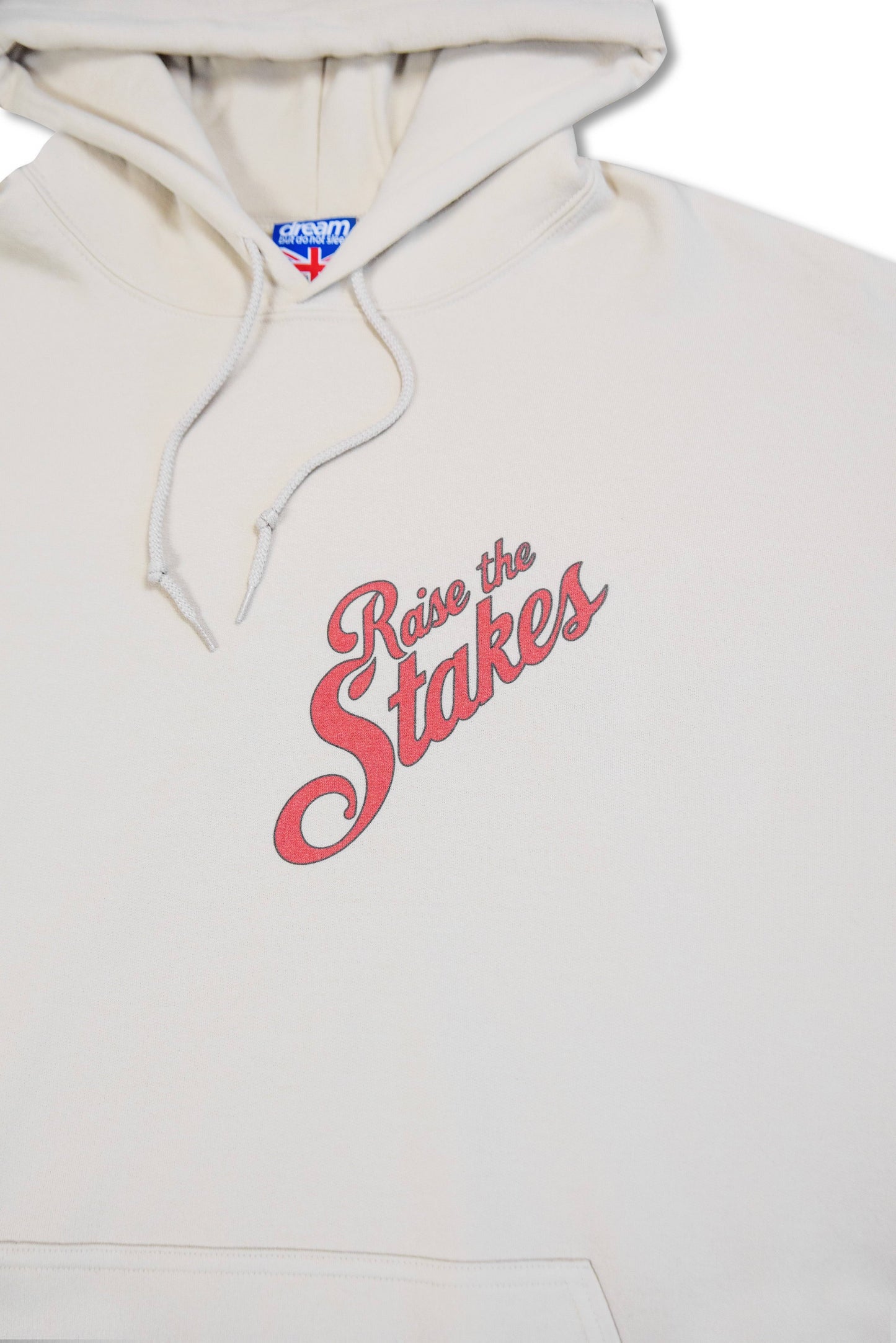 Zoomed-in view of chest print on sand hoodie showing retro red 'Raise the Stakes' text. Soft cotton fabric and drawstring hood.