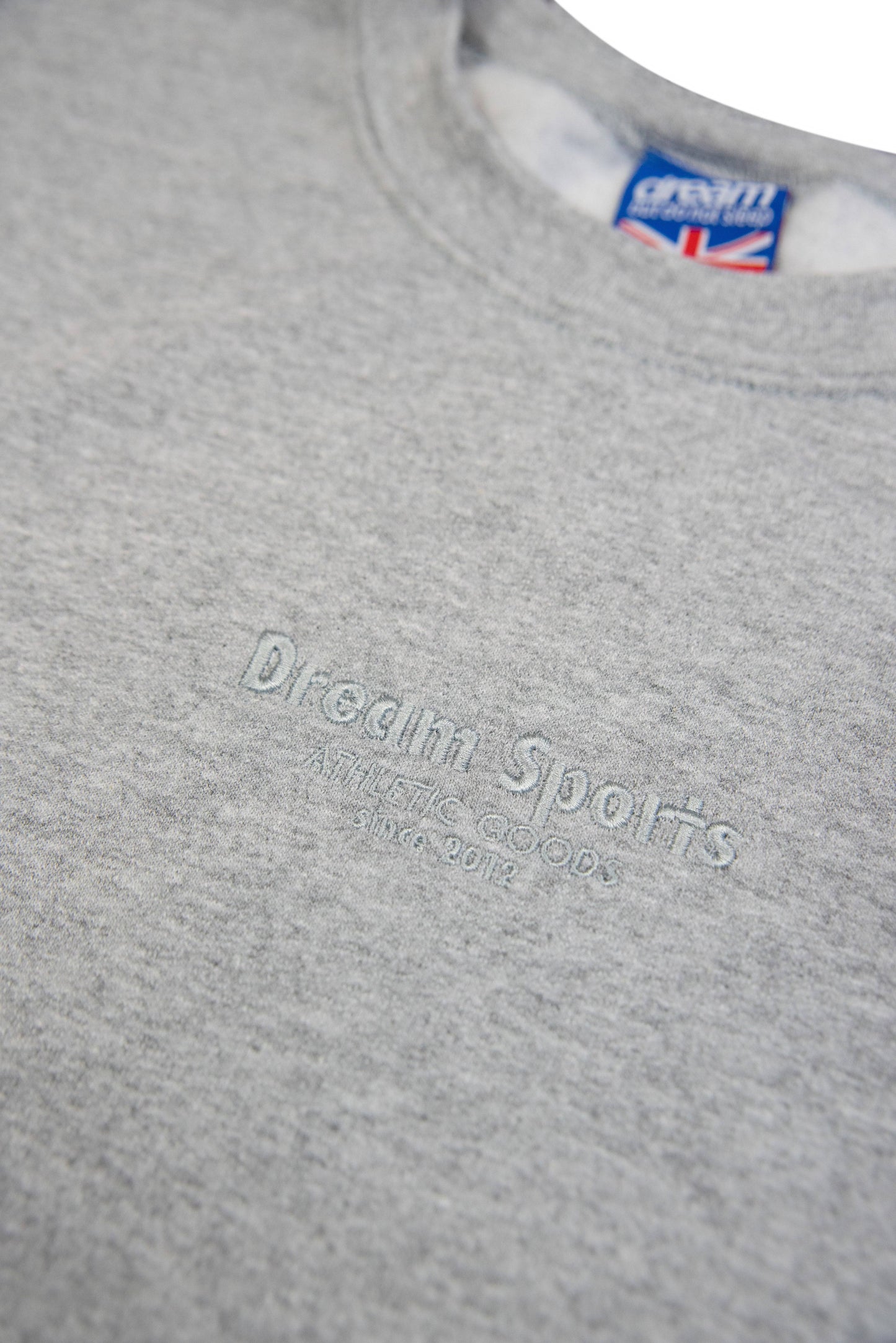 Close-up of tonal Dream Sports embroidery on Heather Grey Sweatshirt, showcasing subtle branding and soft cotton texture.