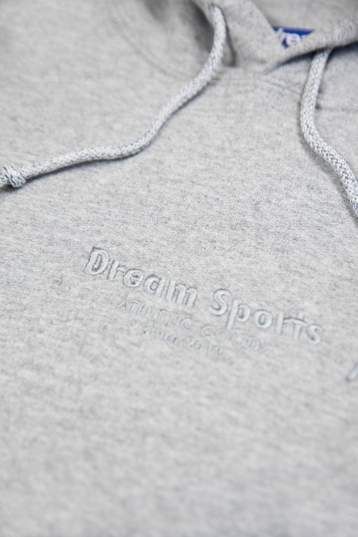 Detailed view of Dream Sports tonal logo embroidery on heather grey hoodie made from heavyweight cotton.
