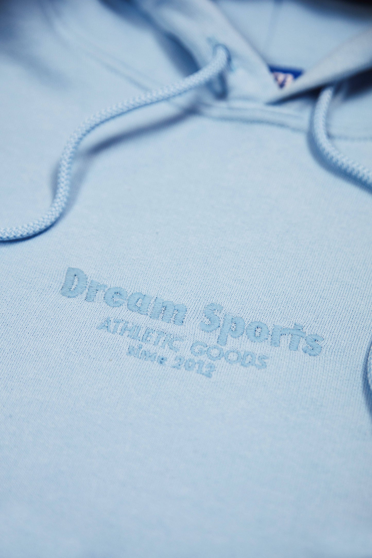 Detailed view of tonal Dream Sports embroidery on unisex blue hoodie, showcasing fine stitching and soft heavyweight cotton fabric.