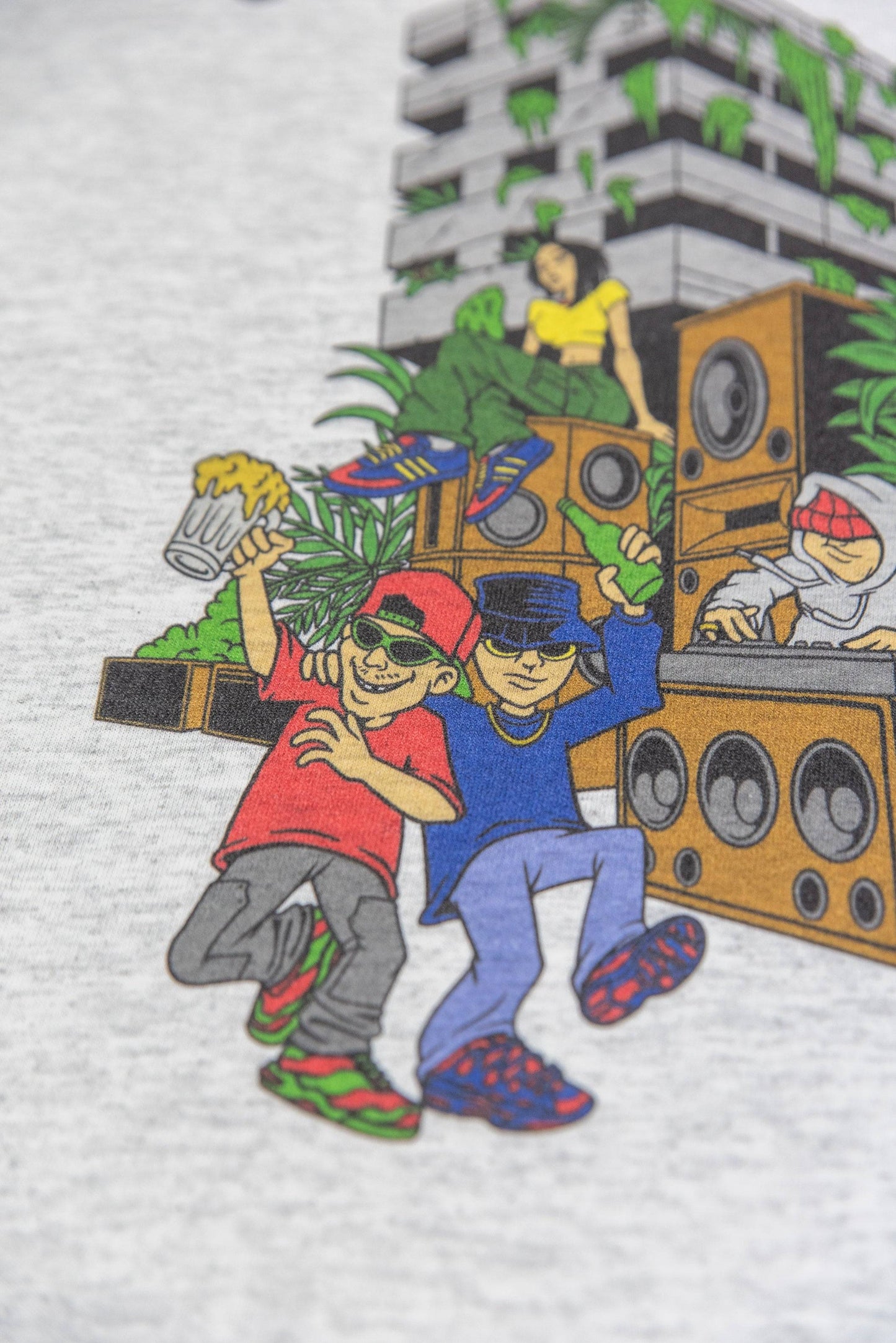 Detail of Ash Grey T-Shirt print with cartoon dancers holding drinks in front of jungle-themed sound system and building.