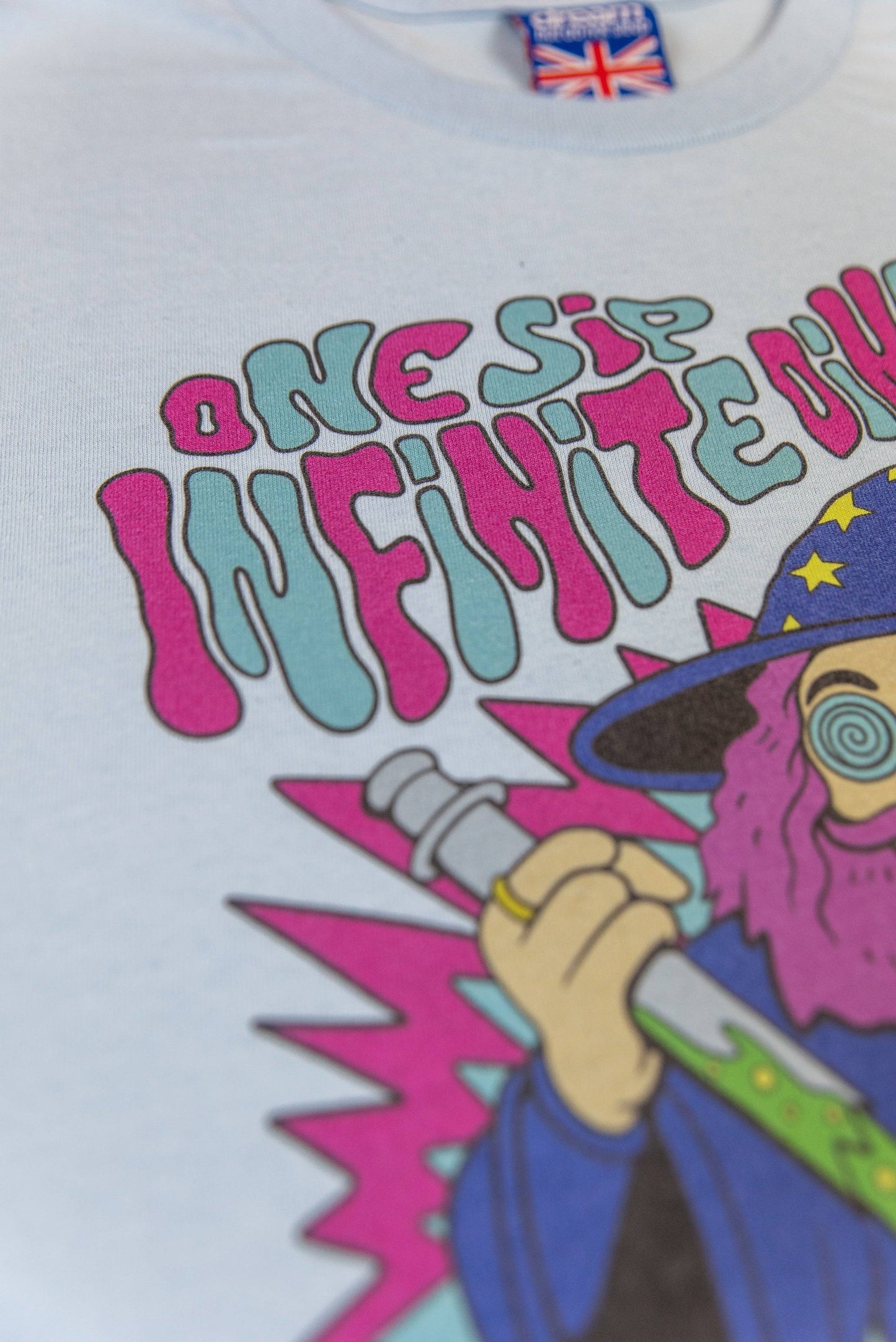Angled close-up of 'One Sip Infinite Dimensions' text on Light Blue T-Shirt Unisex, highlighting colorful psychedelic design.