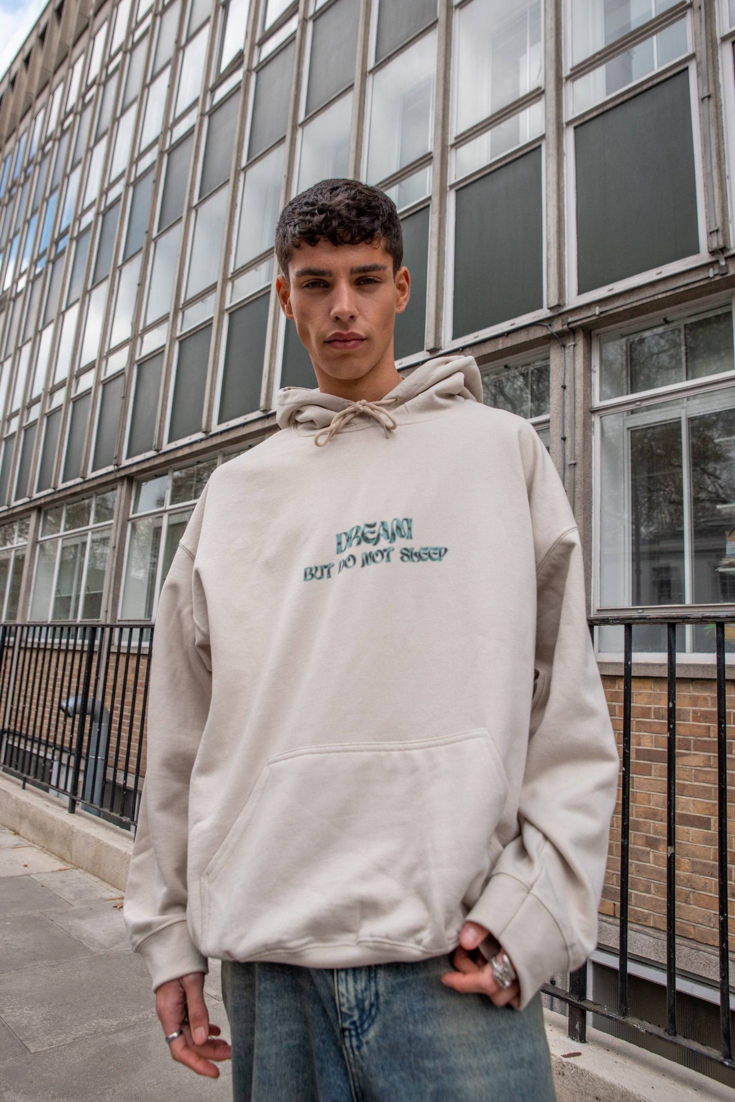 Unisex Hoodie in Sand with cursive 'Dream But Do Not Sleep' logo, heavyweight cotton, styled with relaxed fit for streetwear appeal.