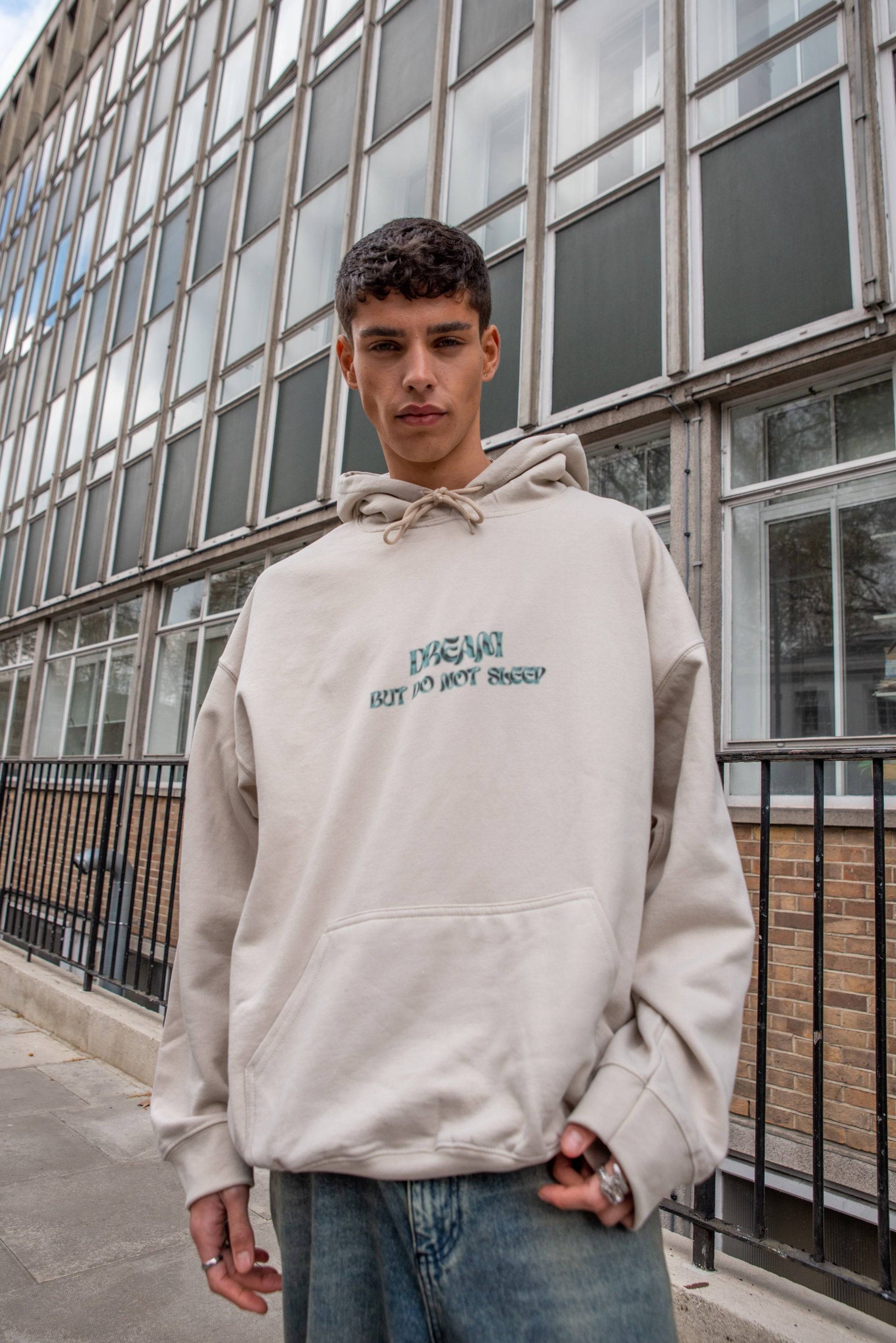 Unisex Hoodie in Sand with cursive 'Dream But Do Not Sleep' logo, heavyweight cotton, styled with relaxed fit for streetwear appeal.