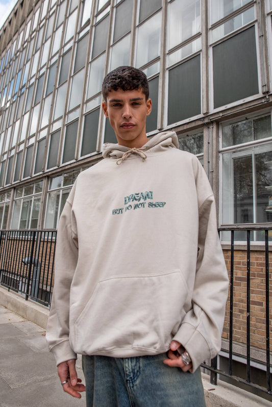 Unisex Hoodie in Sand with cursive 'Dream But Do Not Sleep' logo, heavyweight cotton, styled with relaxed fit for streetwear appeal.