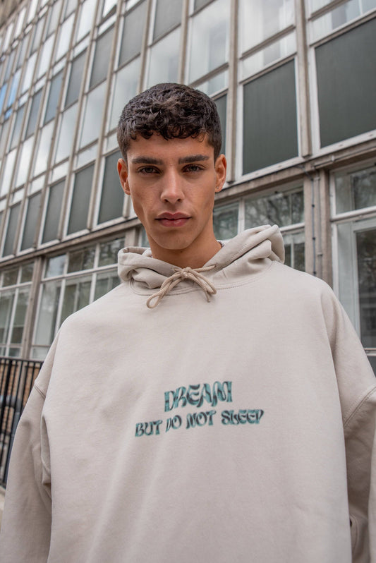Close-up of Hoodie in Sand showcasing embroidered cursive logo print 'Dream But Do Not Sleep' on heavyweight cotton fabric.